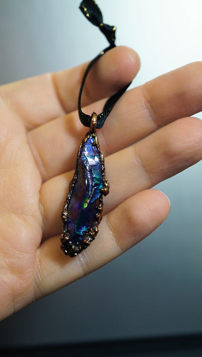 rainbow blues fill this titanium quartz ornament. hung on black ribbon, in hand, against dark background