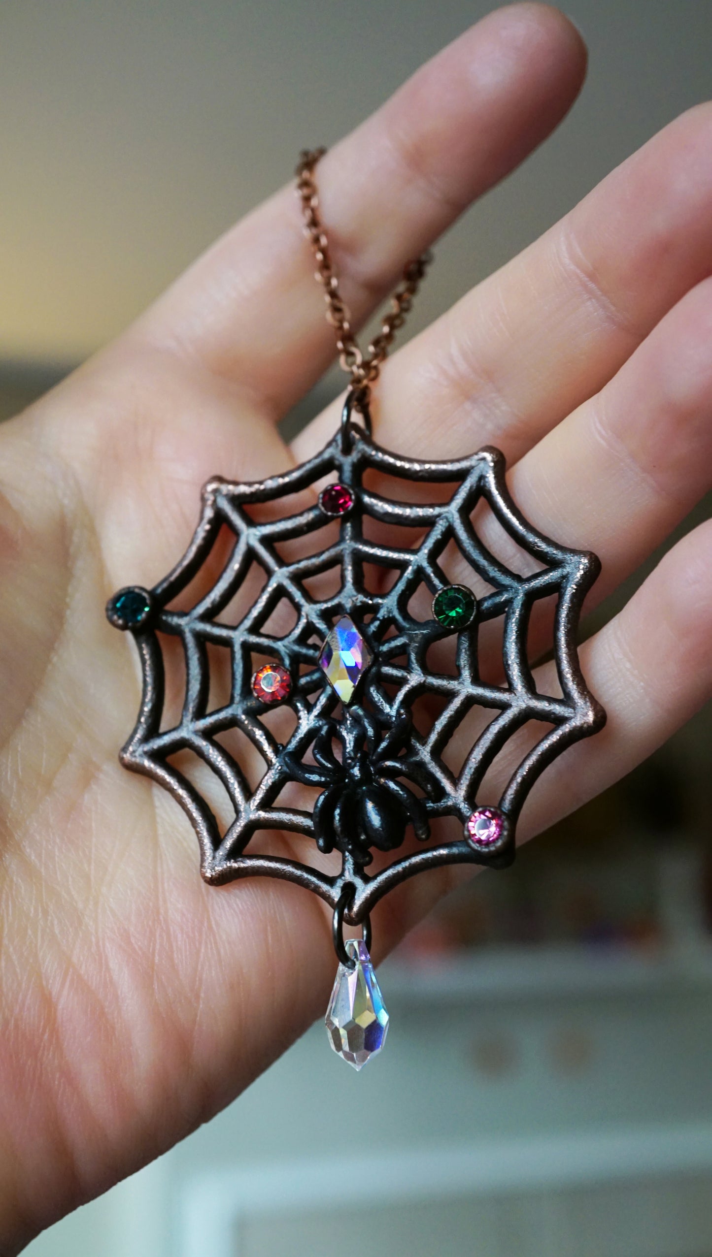 dark copper spiderweb ornament with small christmas light rhinestones, black spider, held in hand with crystal drop dangling 