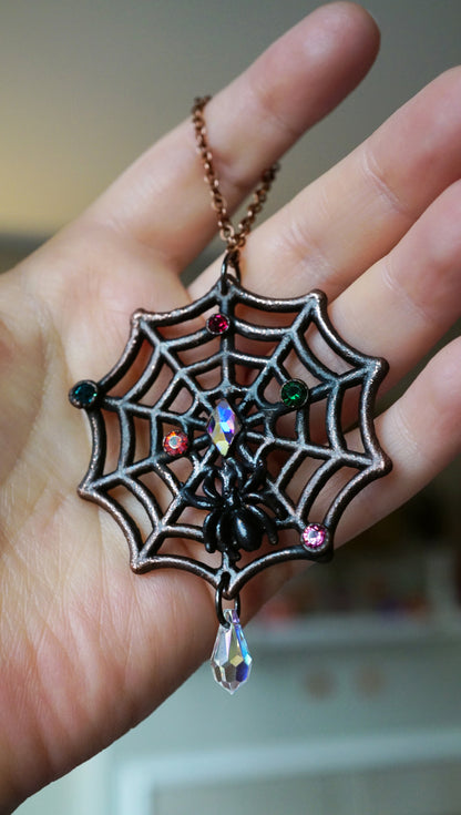 dark copper spiderweb ornament with small christmas light rhinestones, black spider, held in hand with crystal drop dangling 