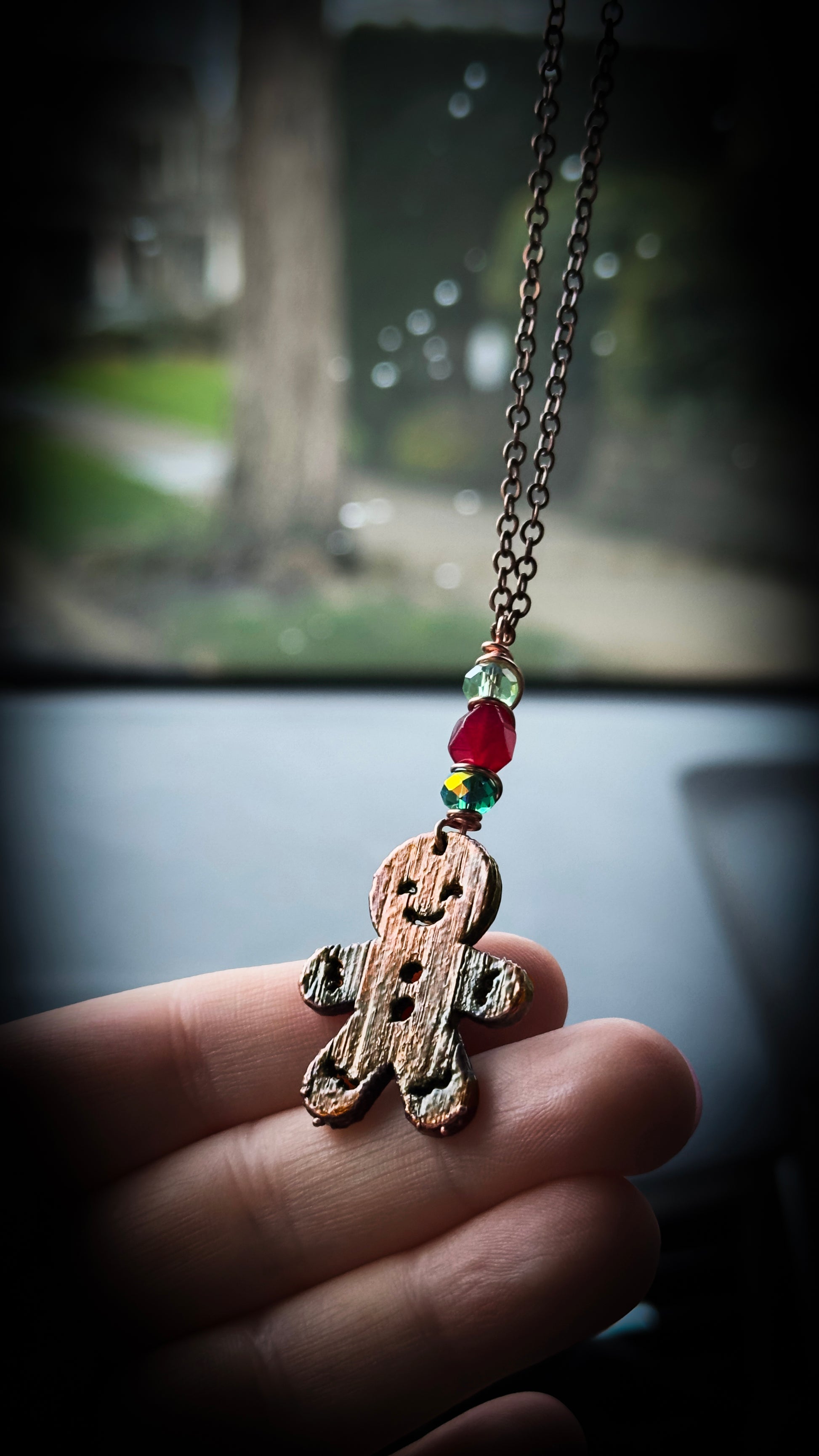 Hand holding a gingerbread man rearview mirror ornament with beads, against a car interior