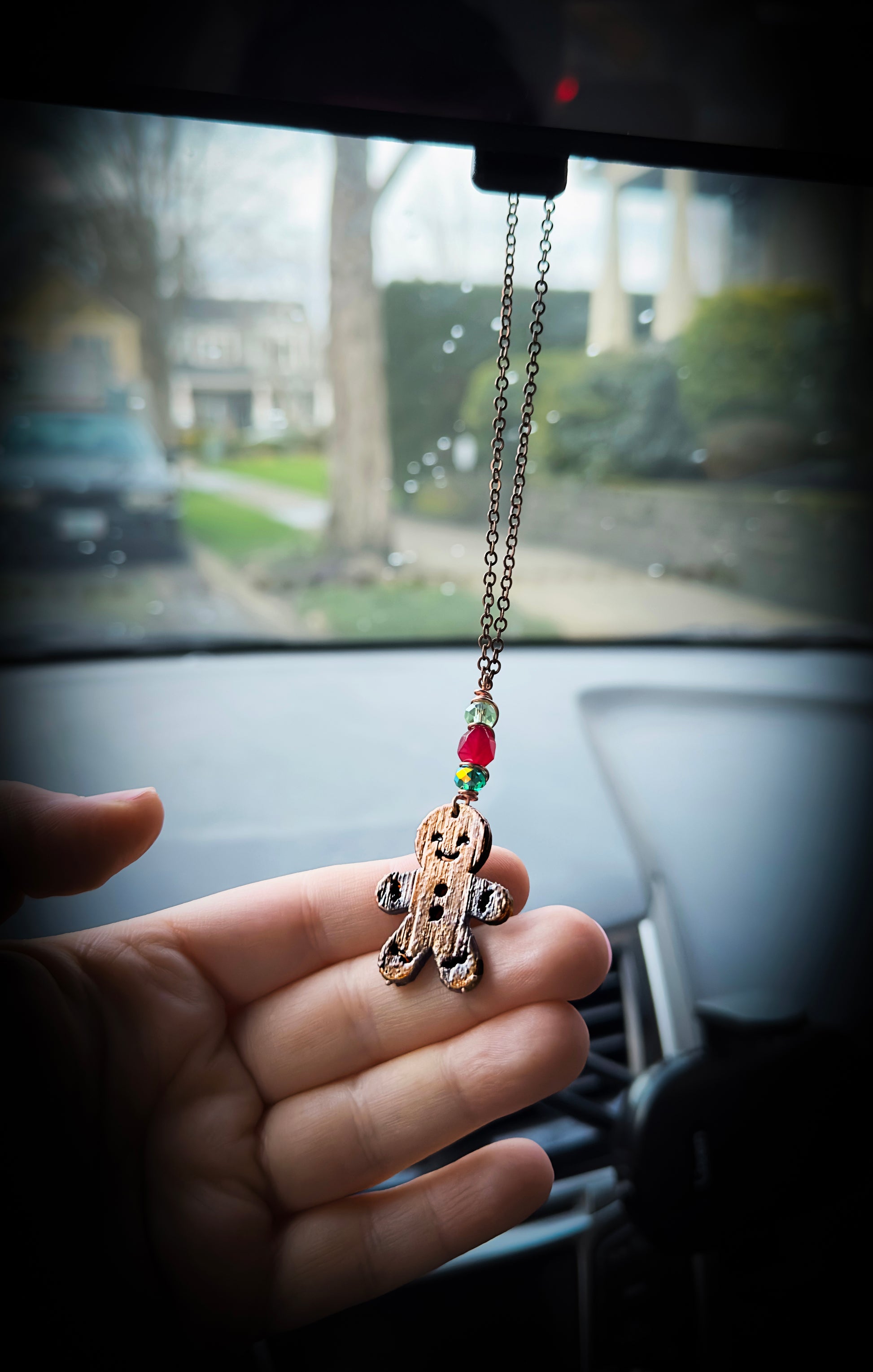 Hand holding a car hanging charm with a blurred car interior background