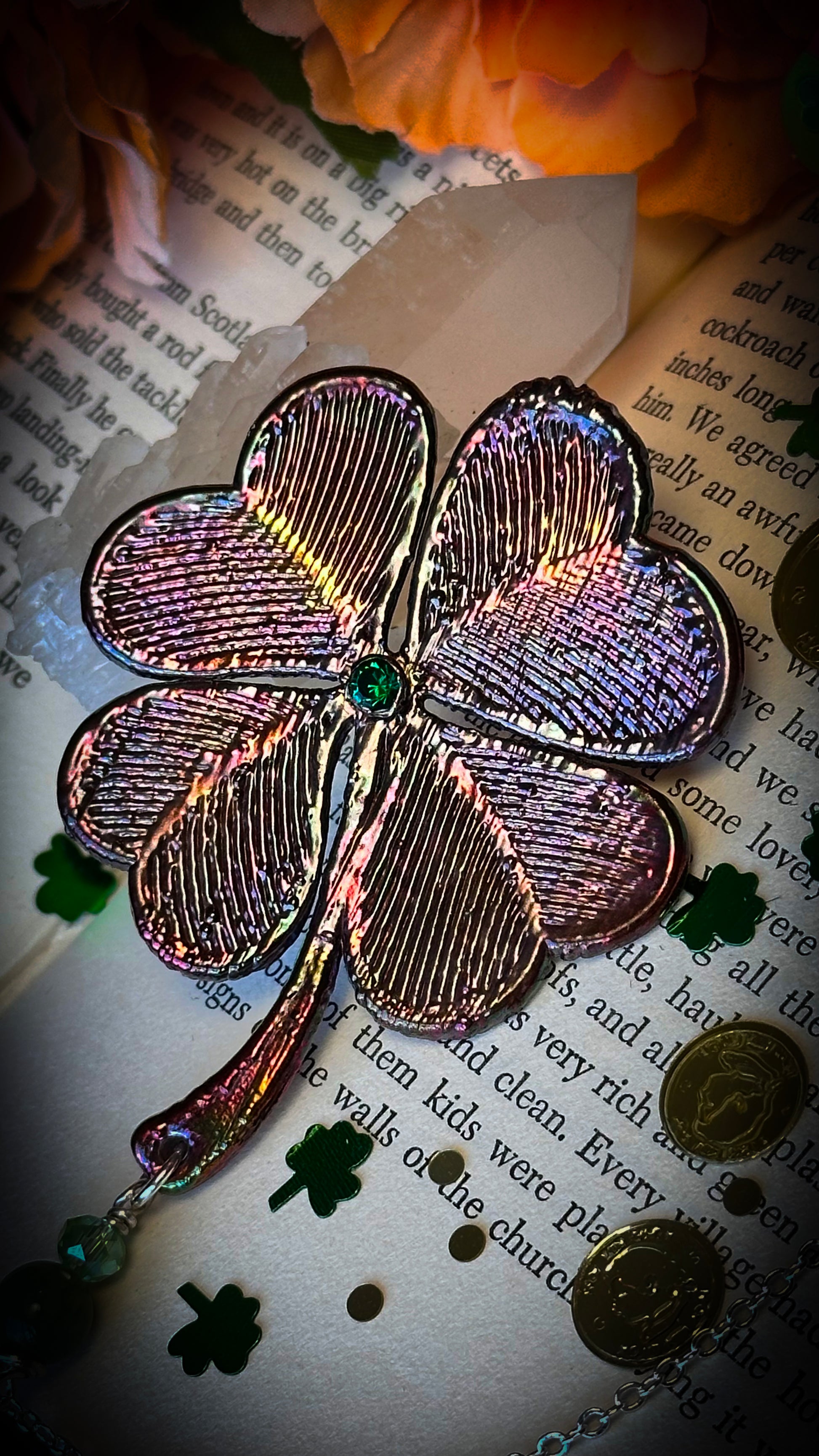 rainbow metallic filigree four leaf clover with green rhinestone in center, against old book with gold coins and shamrocks 