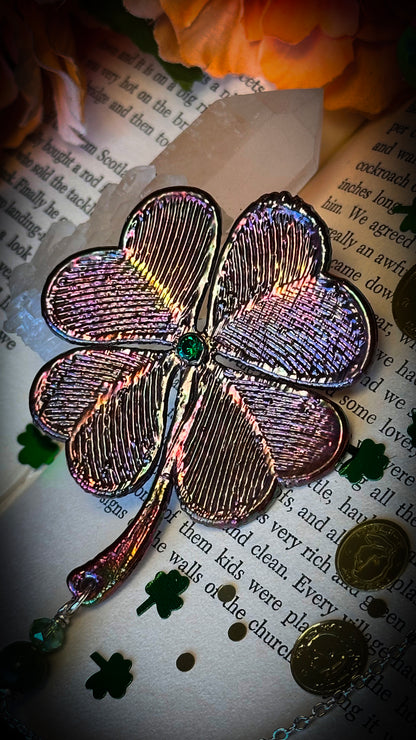 rainbow metallic filigree four leaf clover with green rhinestone in center, against old book with gold coins and shamrocks 
