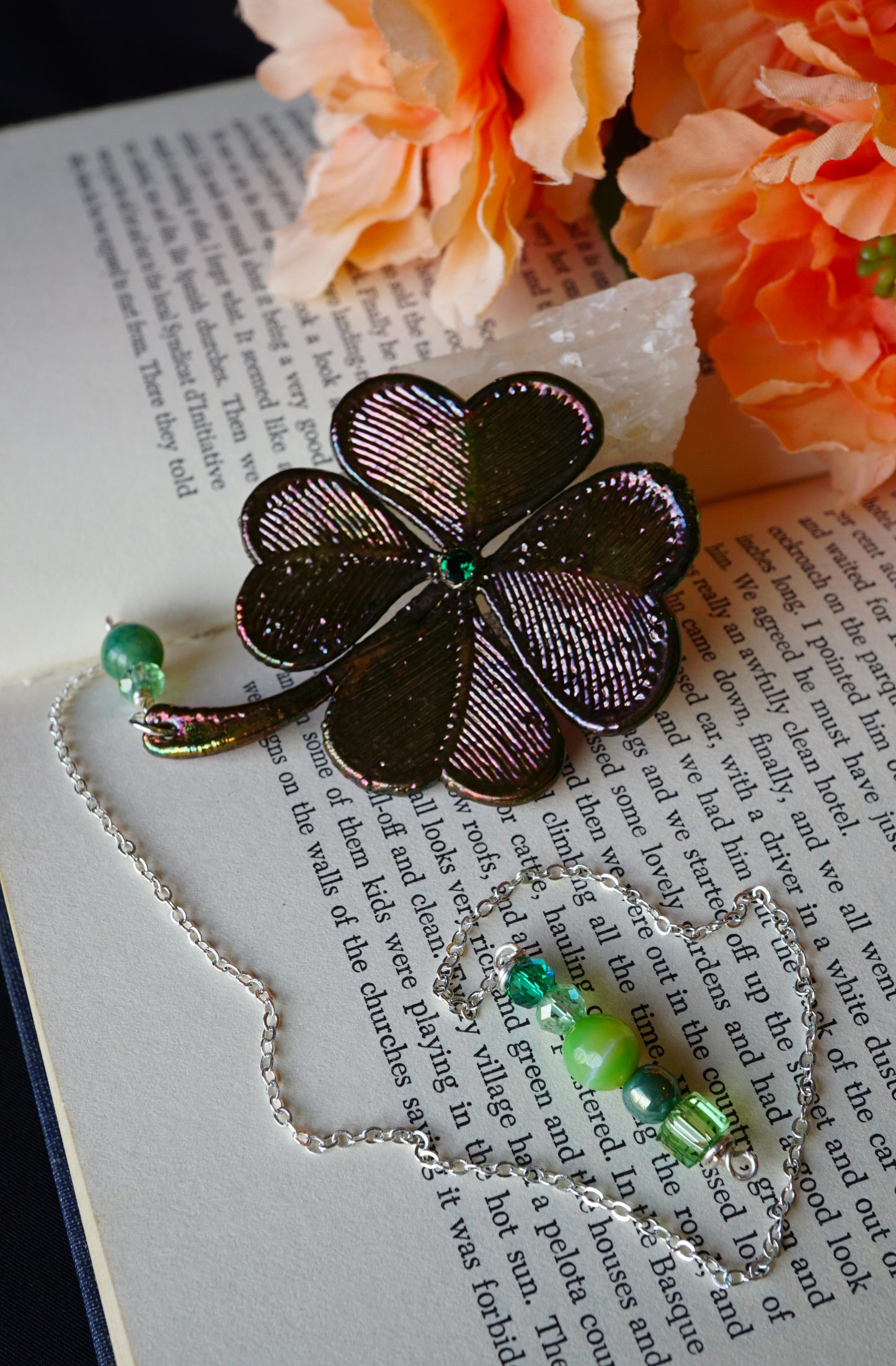 4 leaf clover dark metal with green beads, peach flowers and on book in background
