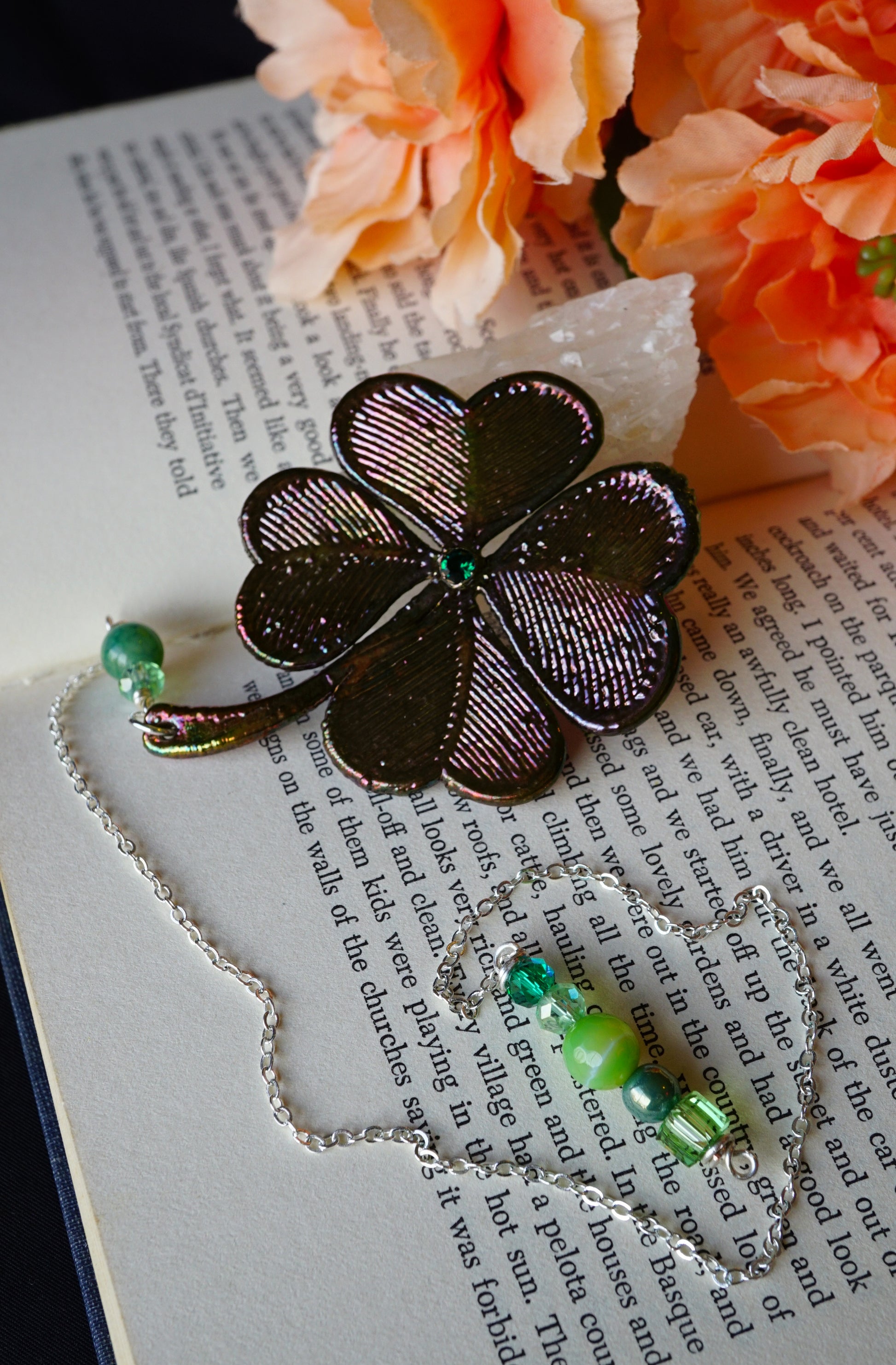 4 leaf clover dark metal with green beads, peach flowers and on book in background