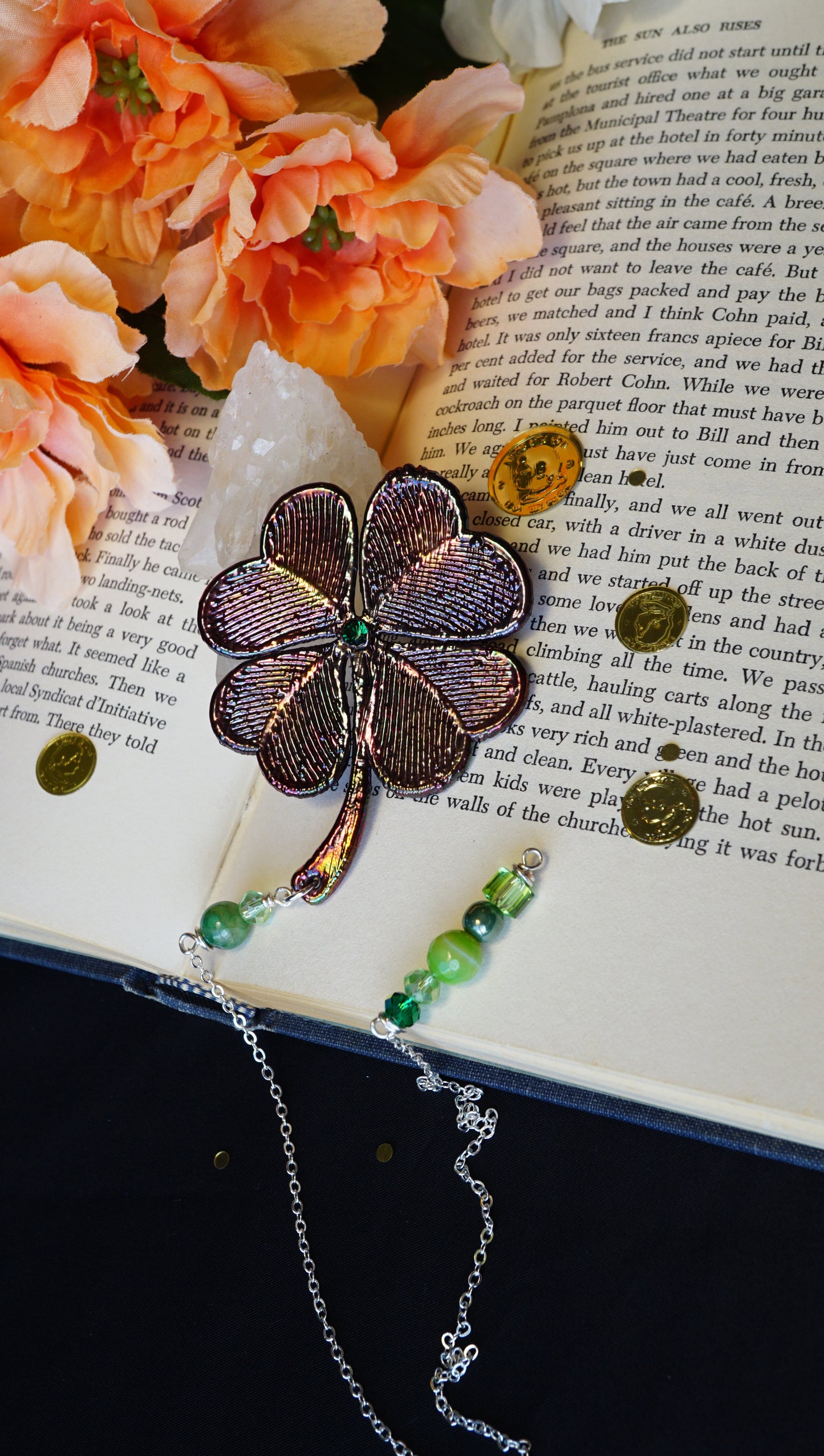 four leaf clover metallic bookmark with dangling green beads, on old book with gold coins and flowers