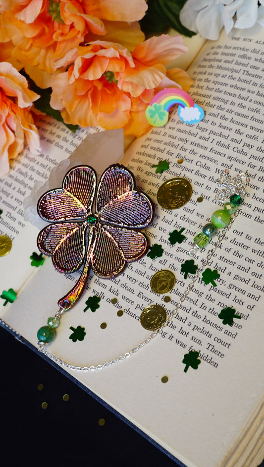 4 leaf clover bookmark with green beaded detail and colorful metallic texture, on old book with gold coins and shamrock confetti, peach colored flowers