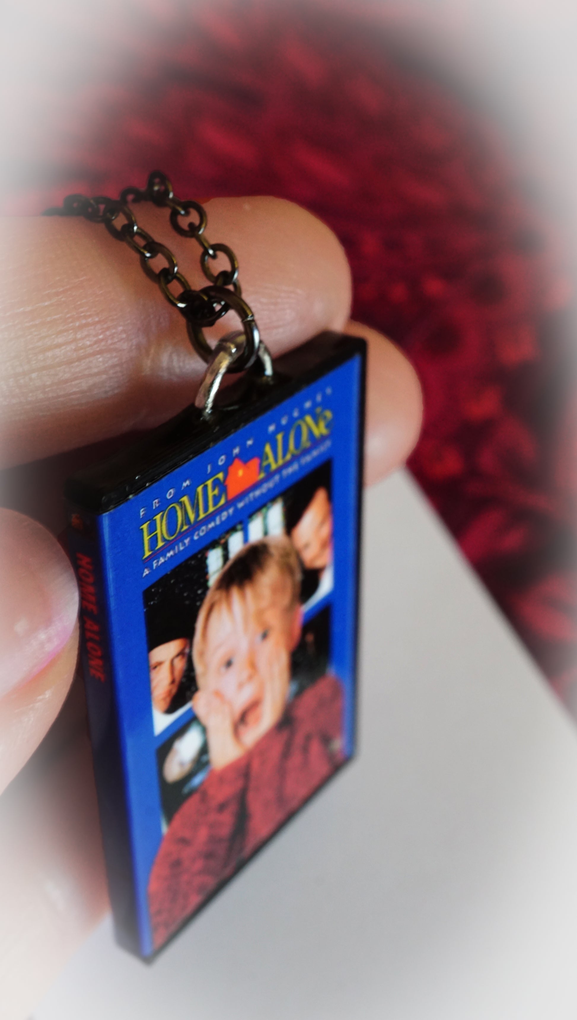 close up of miniature Home Alone DVD case necklace, in hands for size, red background for christmas