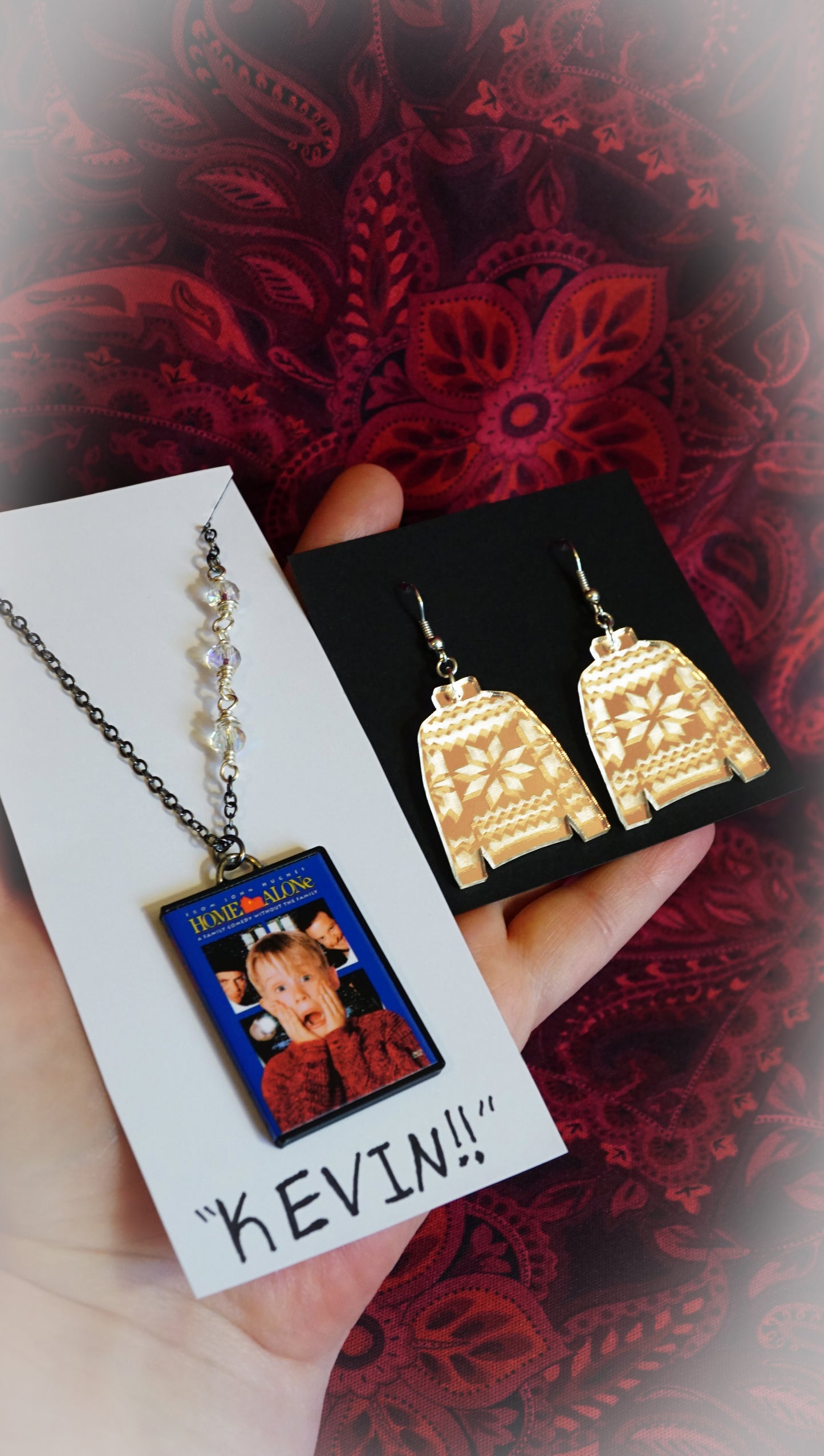 sweater earrings and home alone necklace on a "kevin!!" card display, red background 