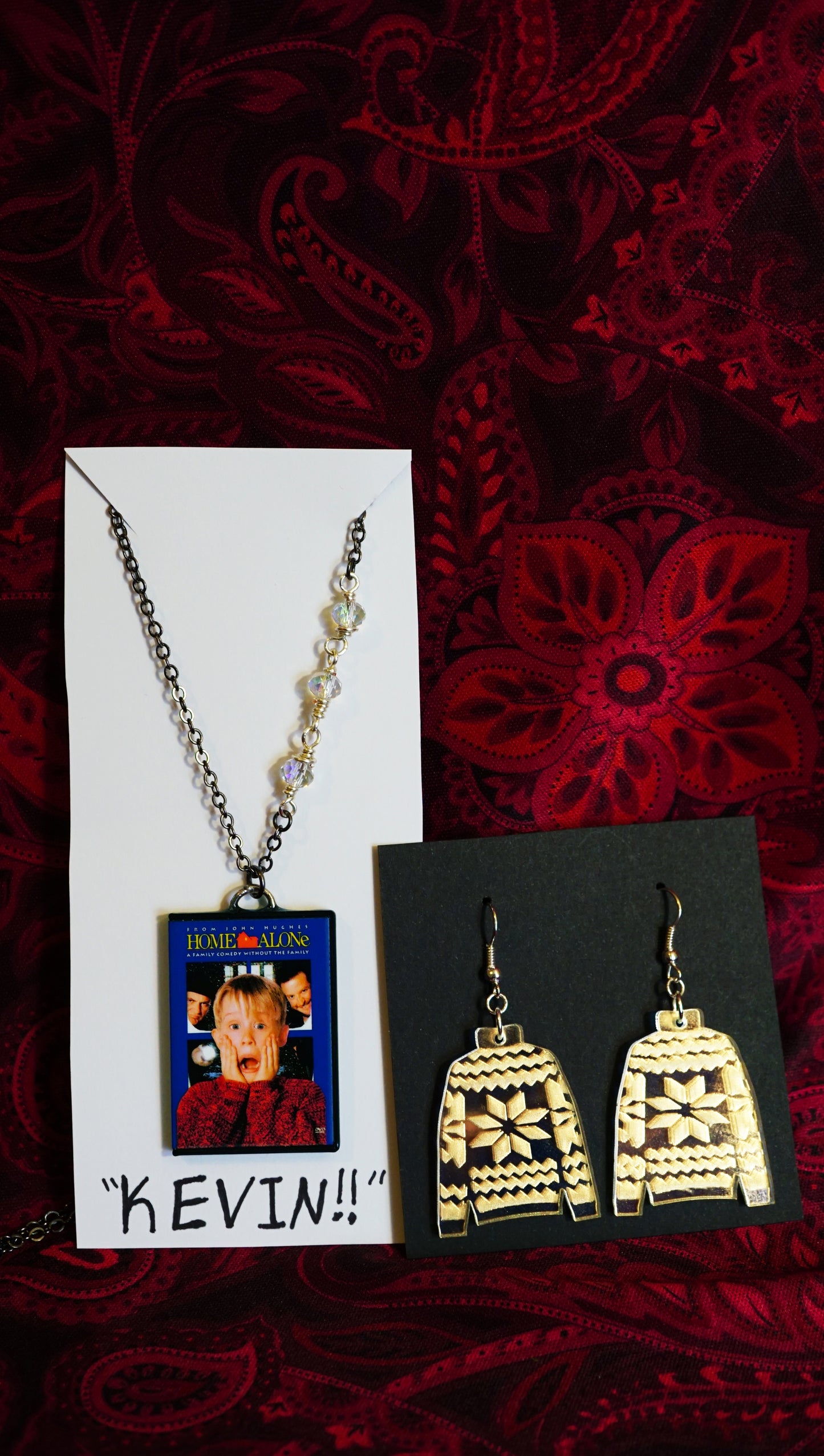 jewelry set with sweater dangles and mini home alone dvd case necklace, on jewelry cards, red background