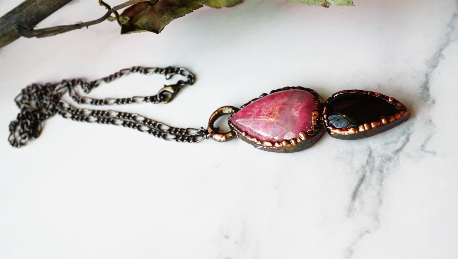 Necklace with pink and black tear drop shaped crystals, finished with black figaro chain, laid flat on a white marble surface