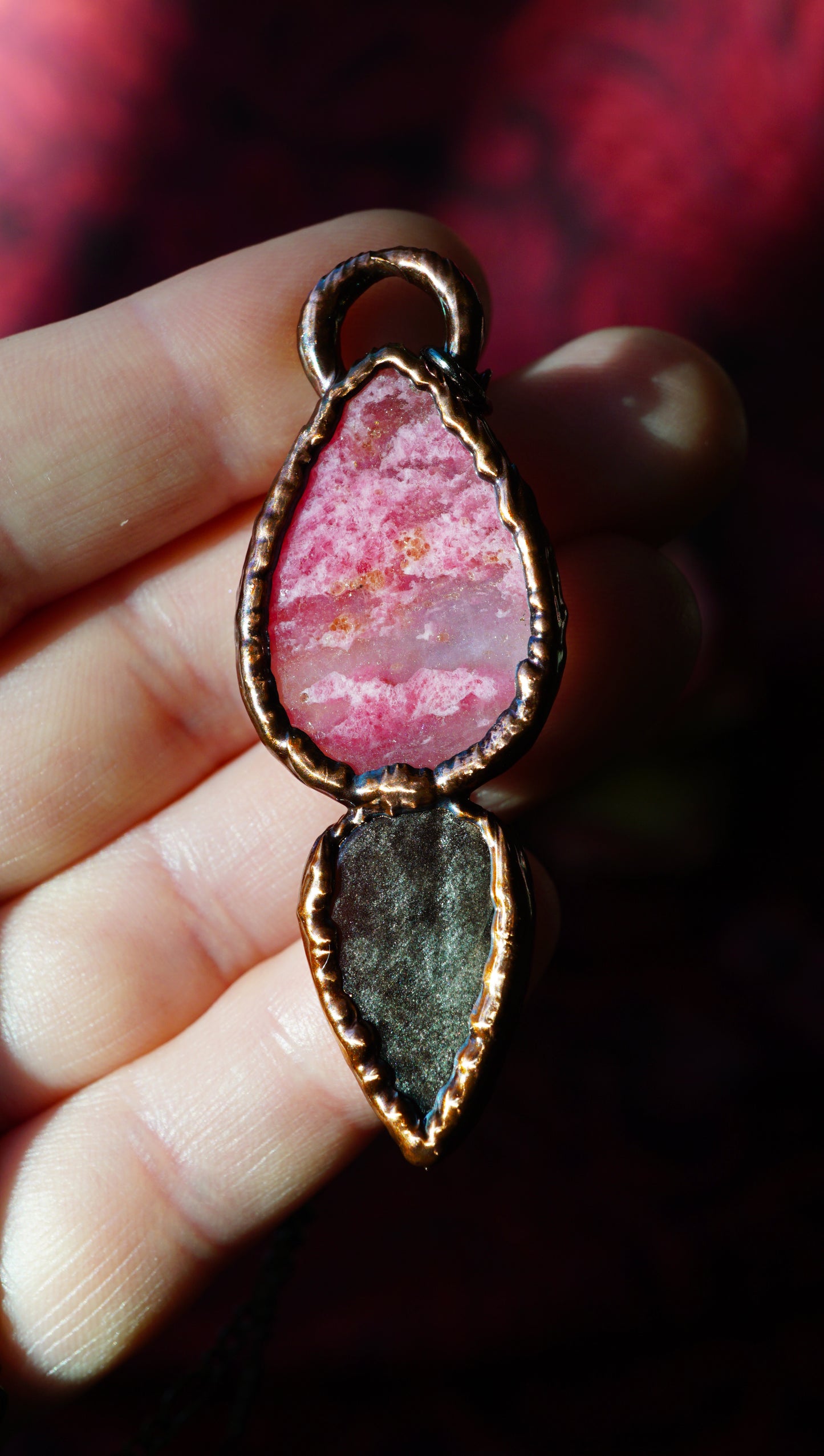 back of a pink and black stone pendant with a patina copper frame held in hand. pink stone looks like pink clouds. obsidian has some silver to it.