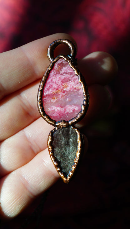 back of a pink and black stone pendant with a patina copper frame held in hand. pink stone looks like pink clouds. obsidian has some silver to it.