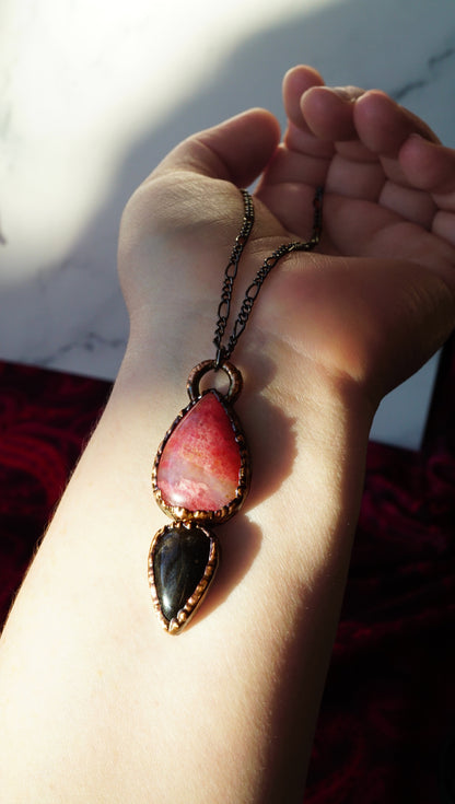 Necklace with pink Rhodonite in Quartz and Black Obsidian on a wrist against a blurred background