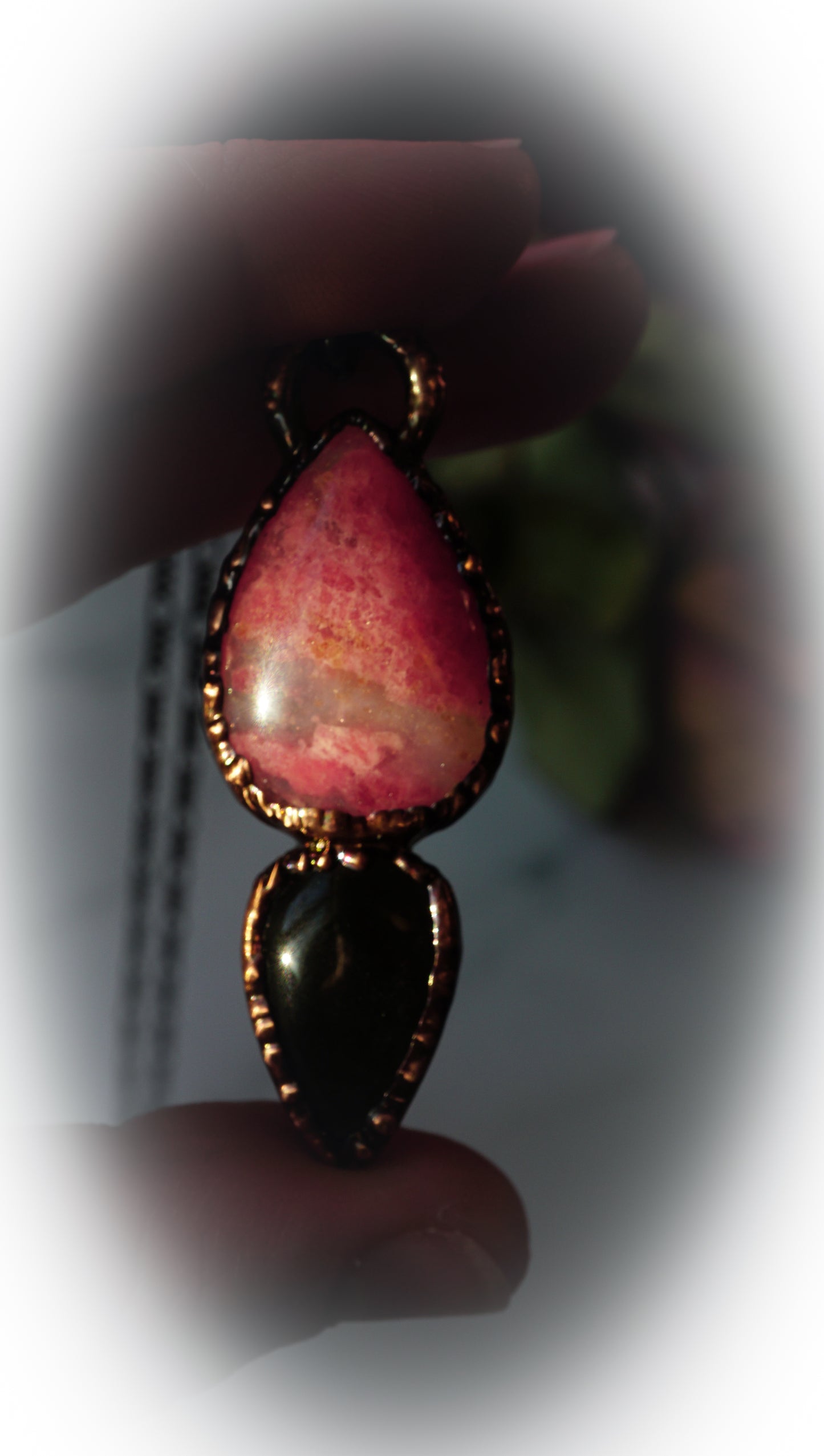 Close-up of a teardrop-shaped pendant with pink and black stones held by a hand.