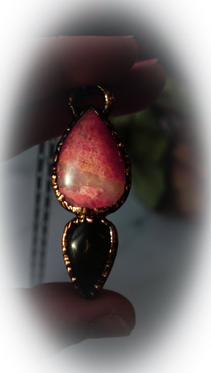 Close-up of a teardrop-shaped pendant with pink and black stones held by a hand.