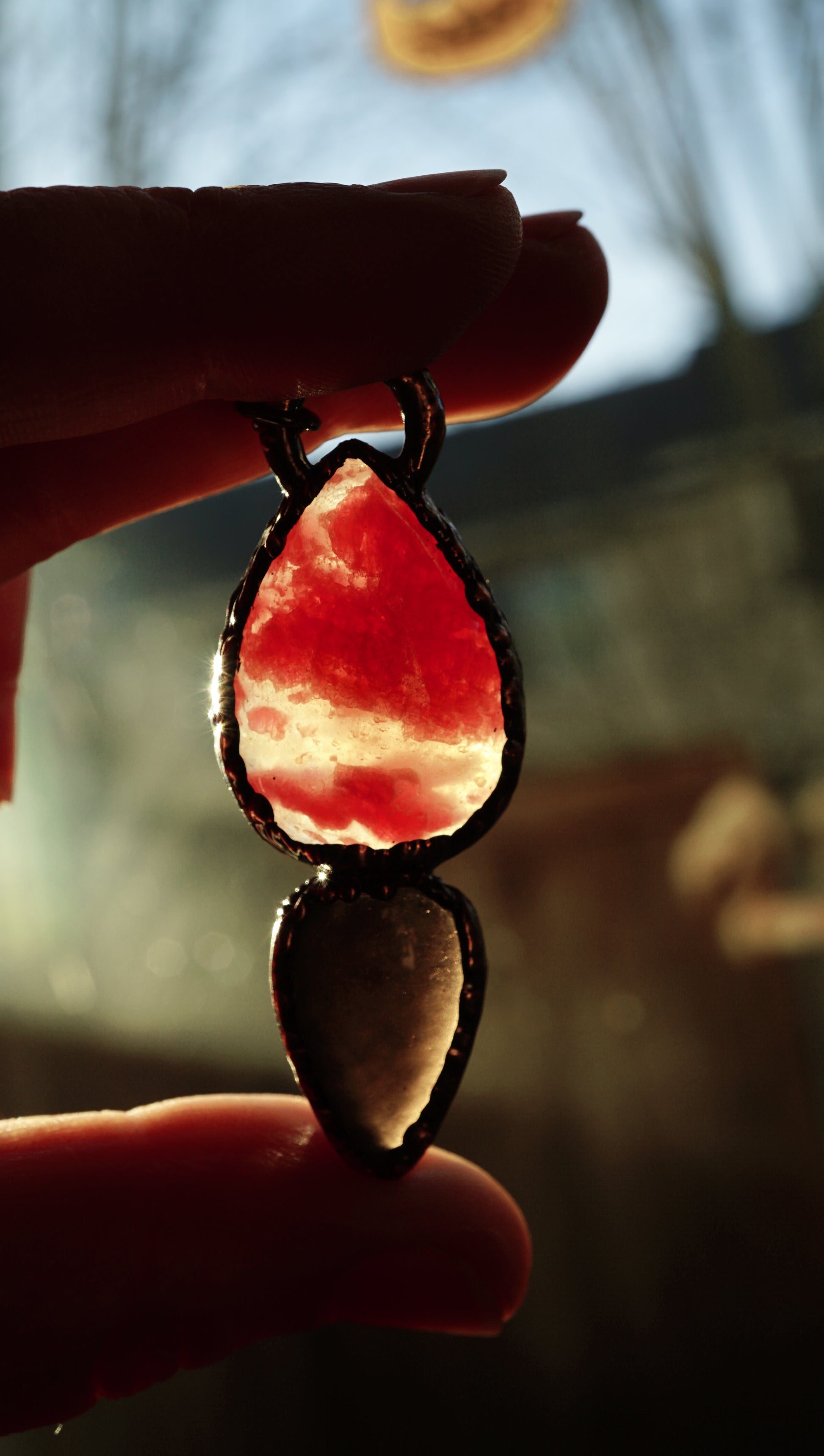 holding a bright pink and black stone pendant against the sun to see through it. 