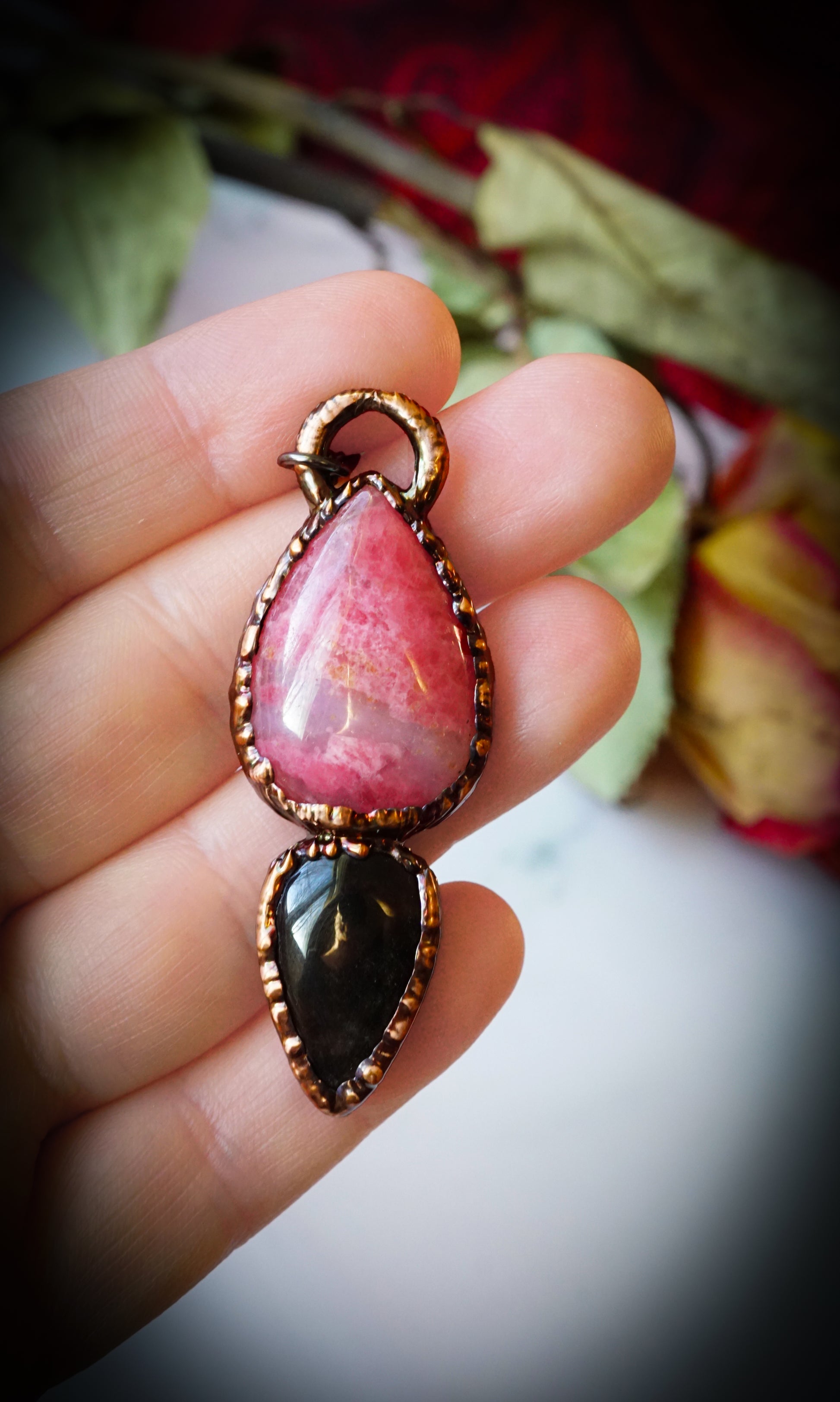 Pink and black teardrop pendant held in a hand with a floral background