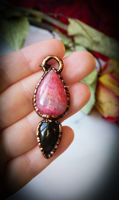 Pink and black teardrop pendant held in a hand with a floral background