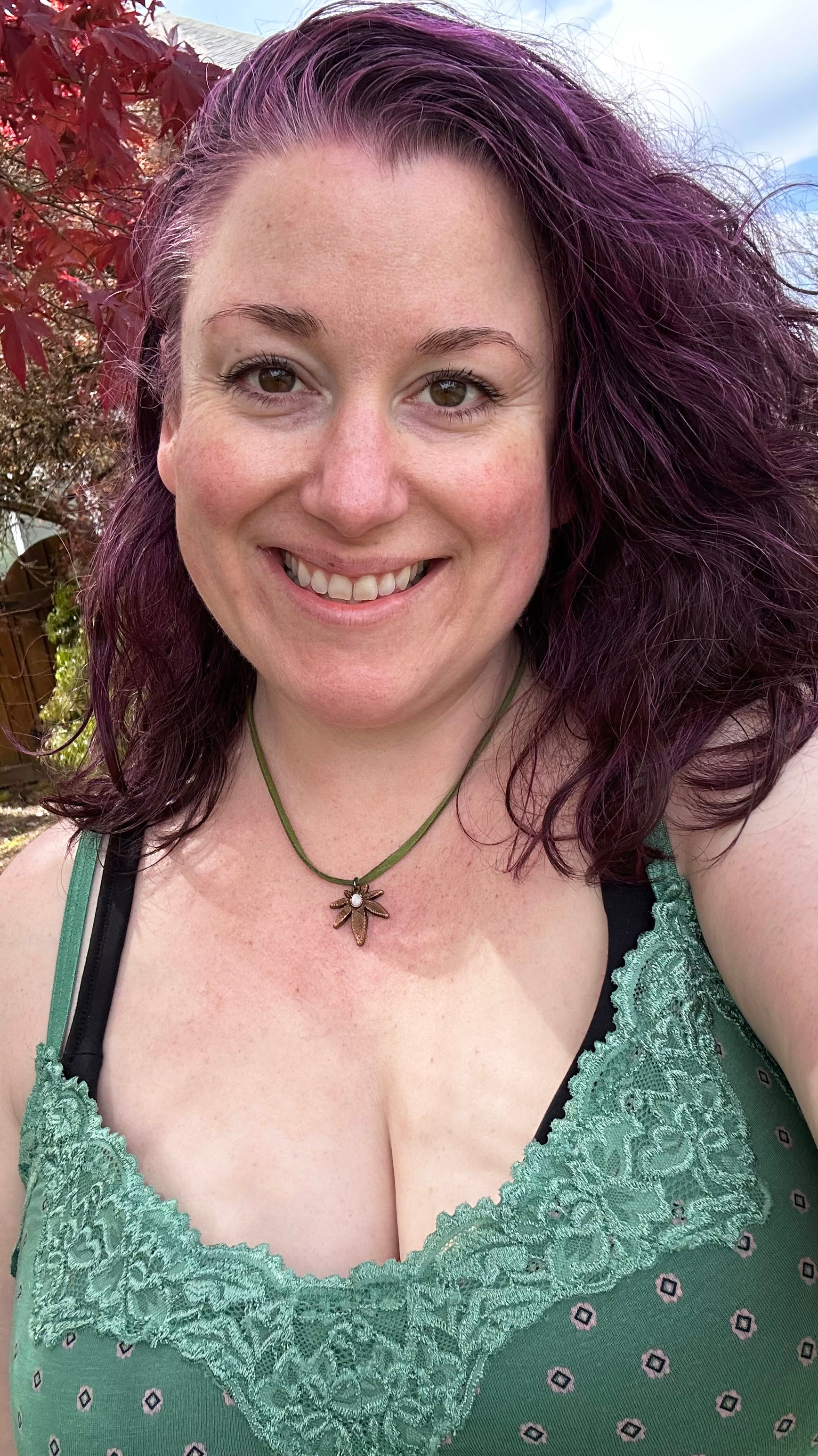Woman with purple hair wearing a green lace top outdoors