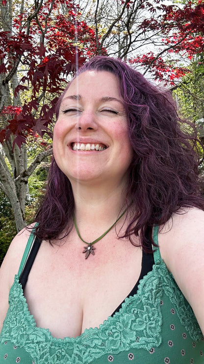Woman with purple hair wearing a copper pot leaf necklace and green lace top, outdoors among trees with red leaves.