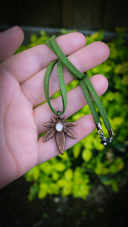 Hand holding a necklace with a marijuana pendant against a blurred green background