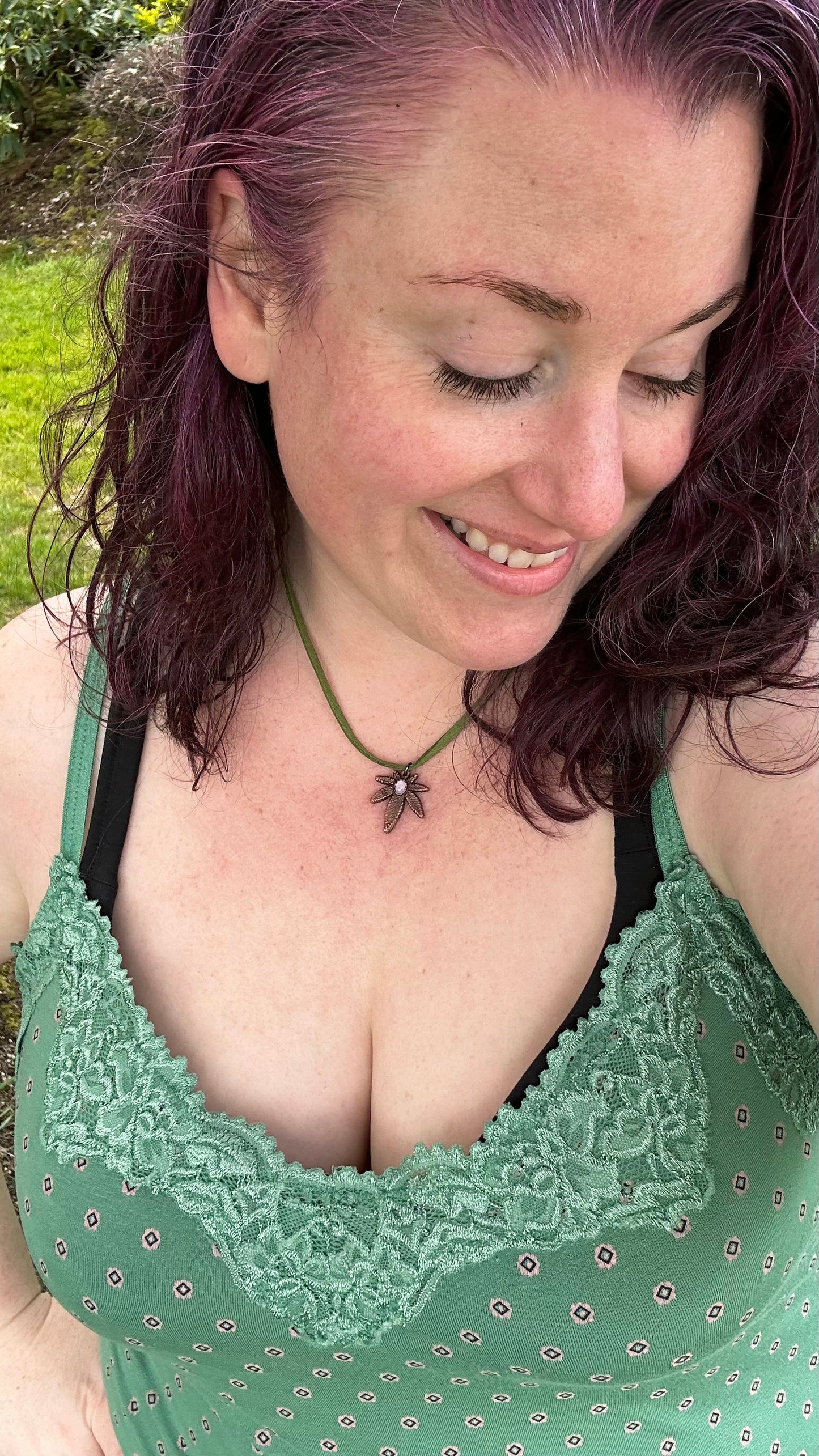 Woman wearing a green lace top and pot leaf necklace outdoors