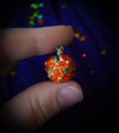orange flower bead necklace, between two fingers, background is an indigo fabric with sparkly rainbow leaf confetti