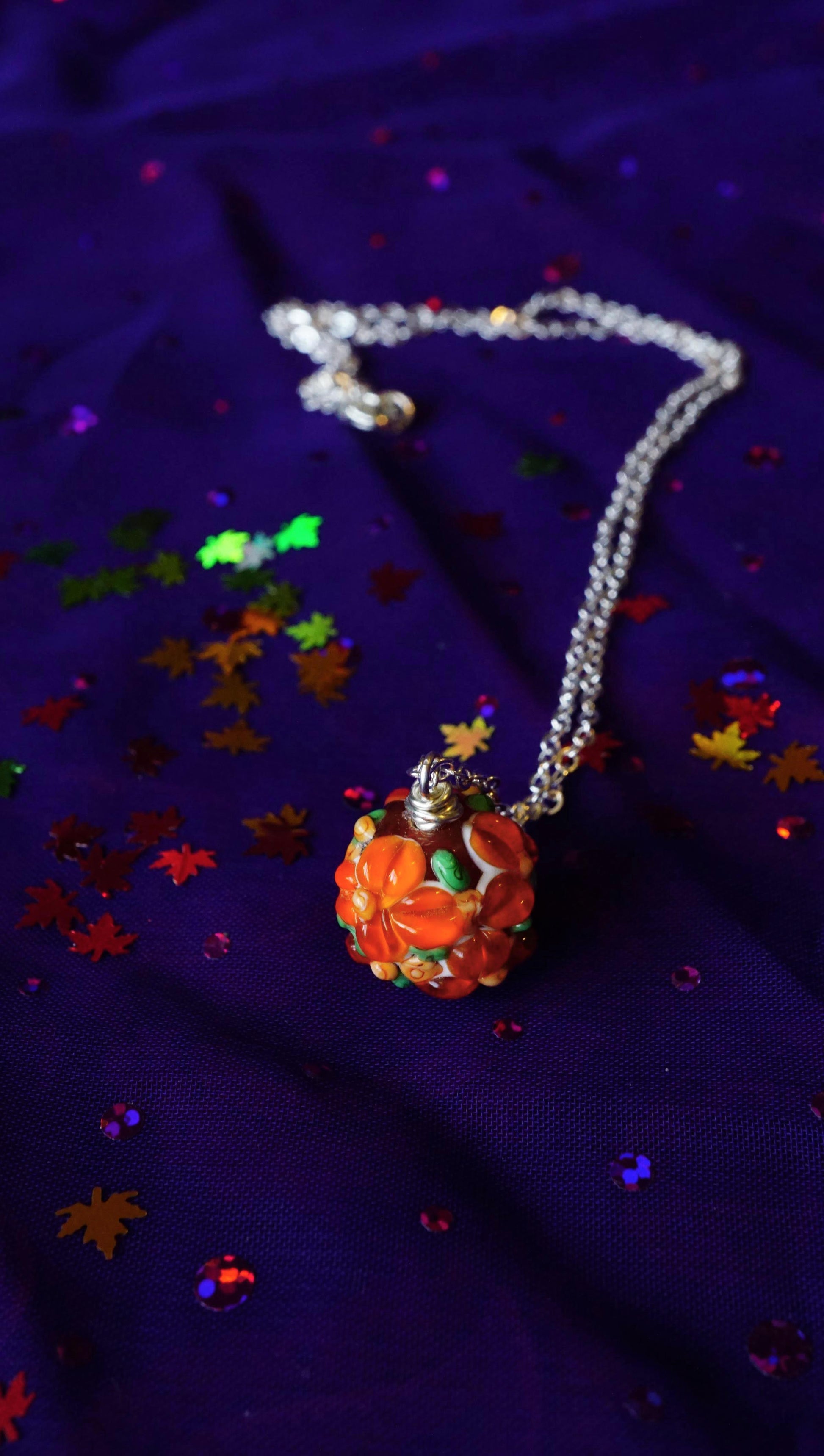 orange floral Necklace on a purple fabric background with colorful leaf confetti.