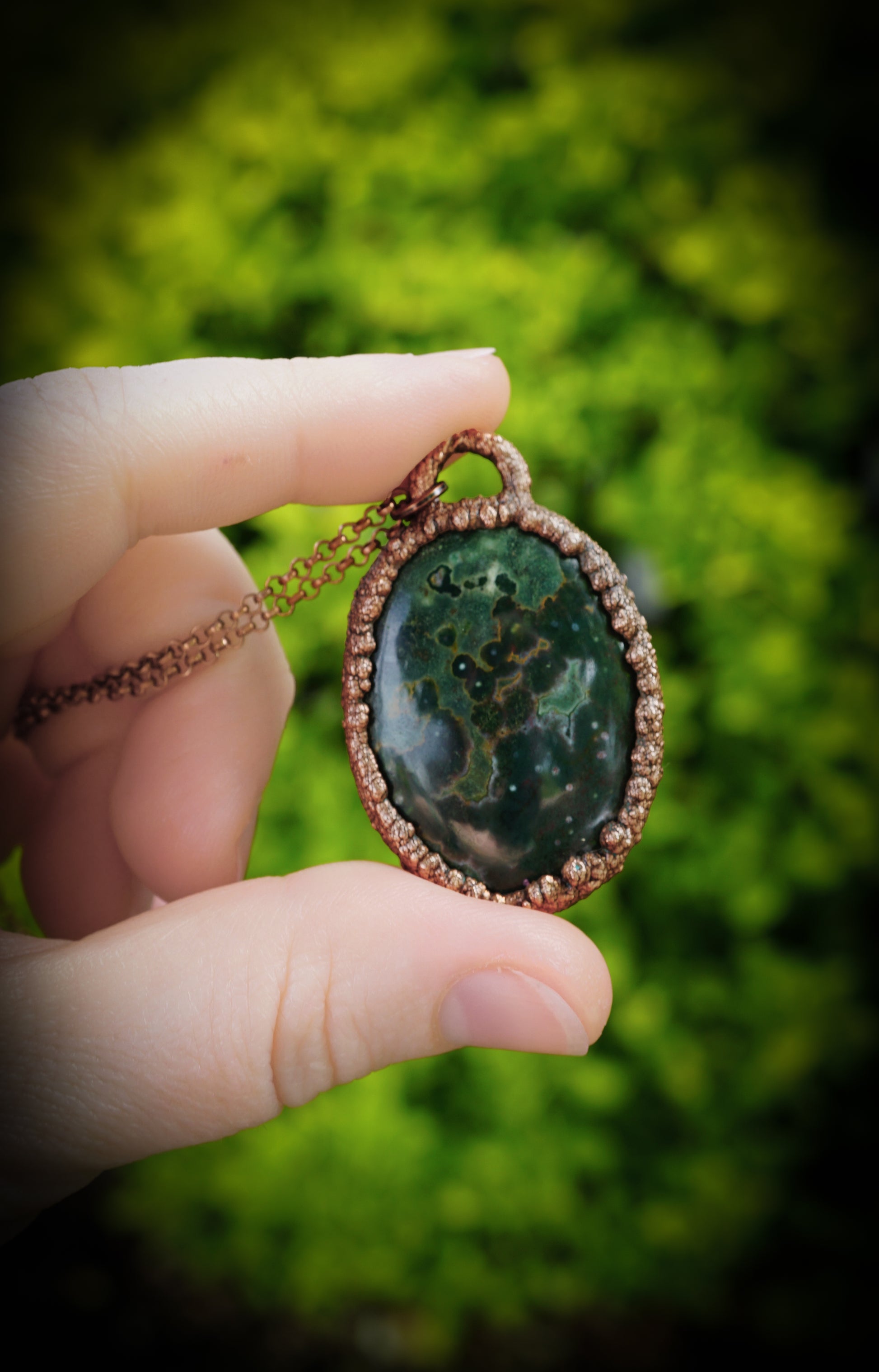 Hand holding a green stone pendant with a blurred green background