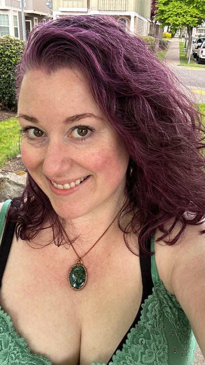 Woman with purple hair wearing a green top and necklace outdoors.