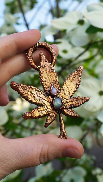 Gold leaf-shaped pendant held by a hand with a blurred green background