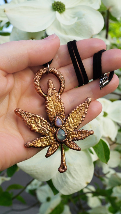 Hand holding a decorative leaf-shaped ornament with a gemstone, against a blurred floral background.