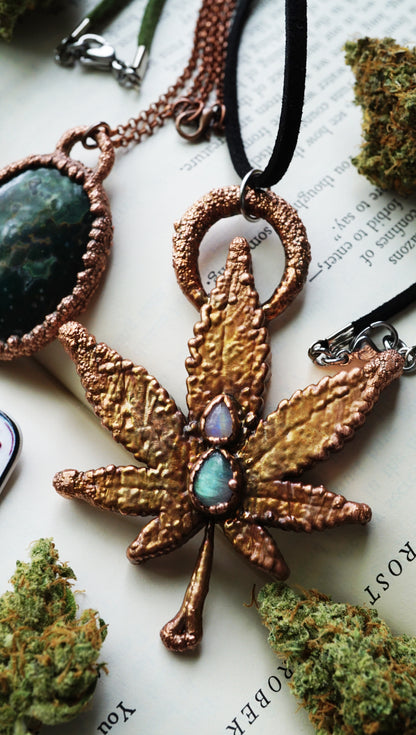 copper cannabis leaf-shaped pendant with green labradorite and moonstone teardrops on book with weed nugs