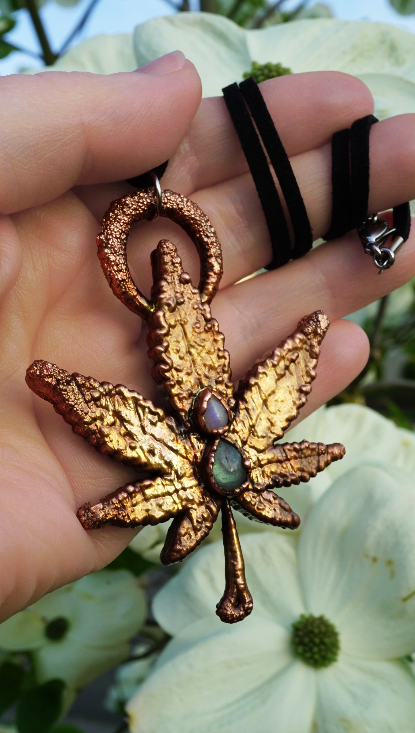 Hand holding a gold-colored pendant with a leaf design against a blurred natural background