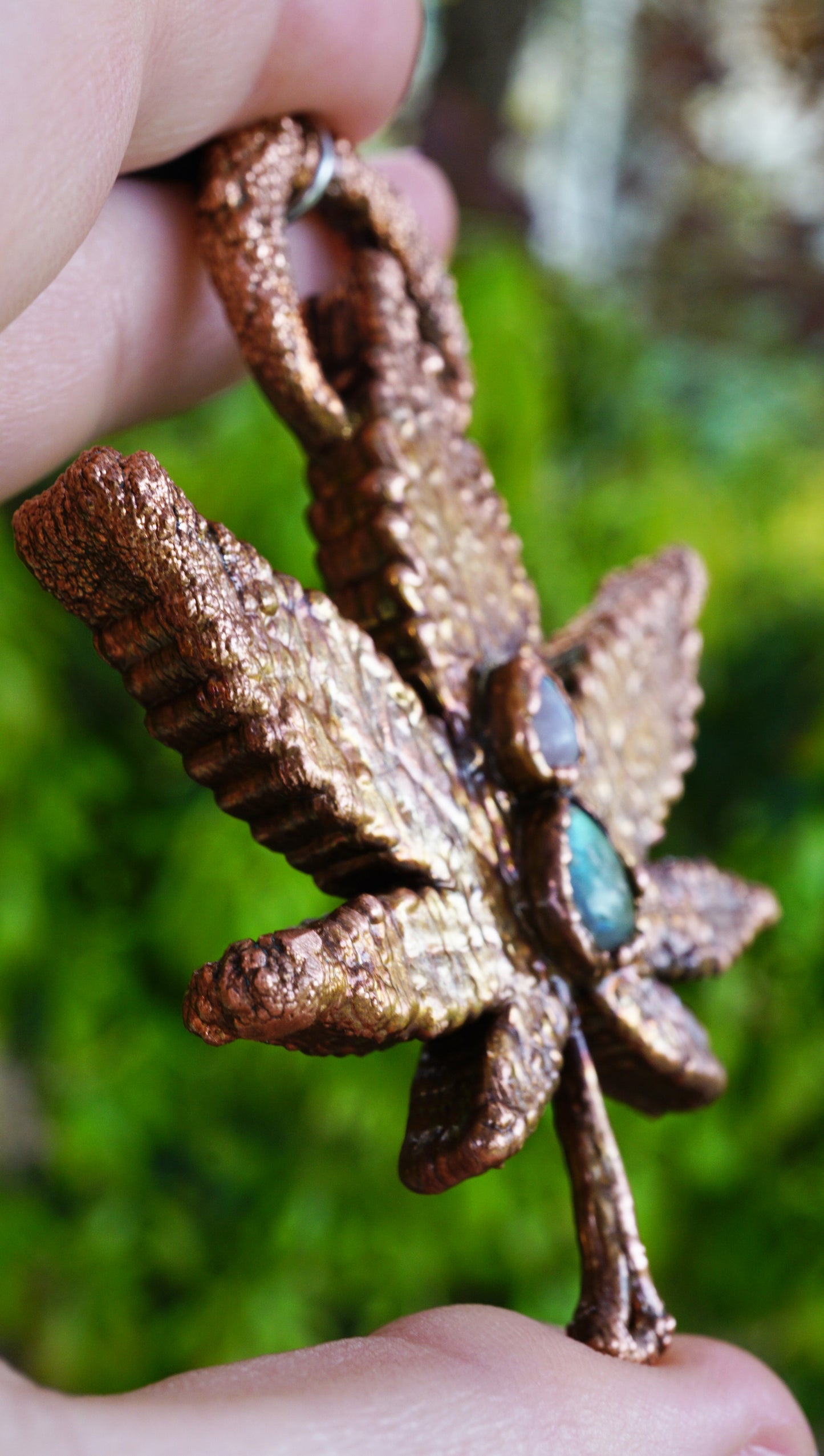 copper leaf necklace with green and white gemstone, in hand against green leaf background