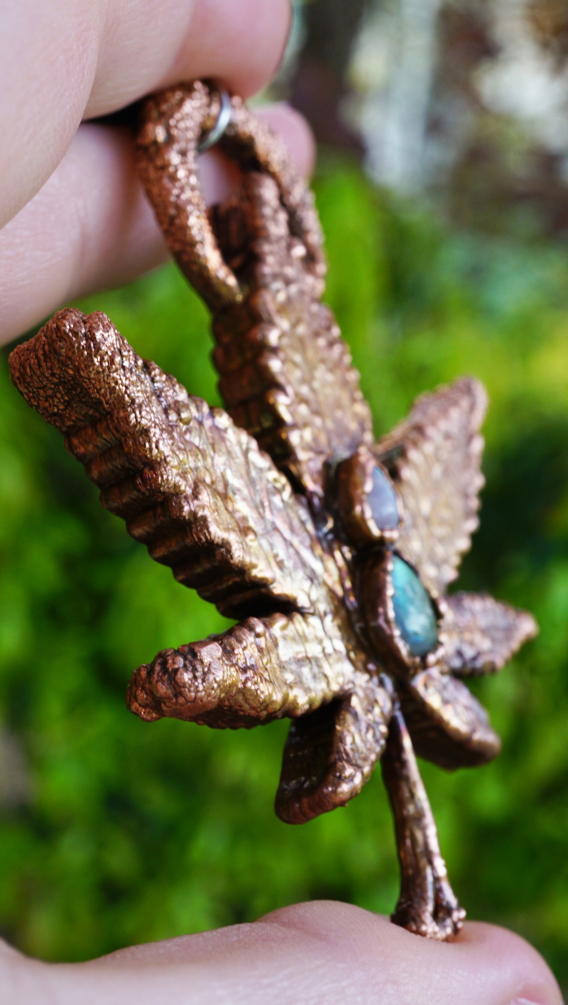 copper leaf necklace with green and white gemstone, in hand against green leaf background