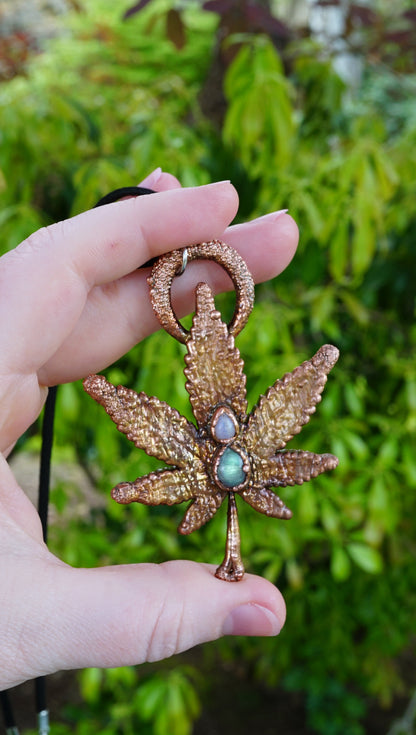 decorative weed leaf necklace in hands against green leaf background