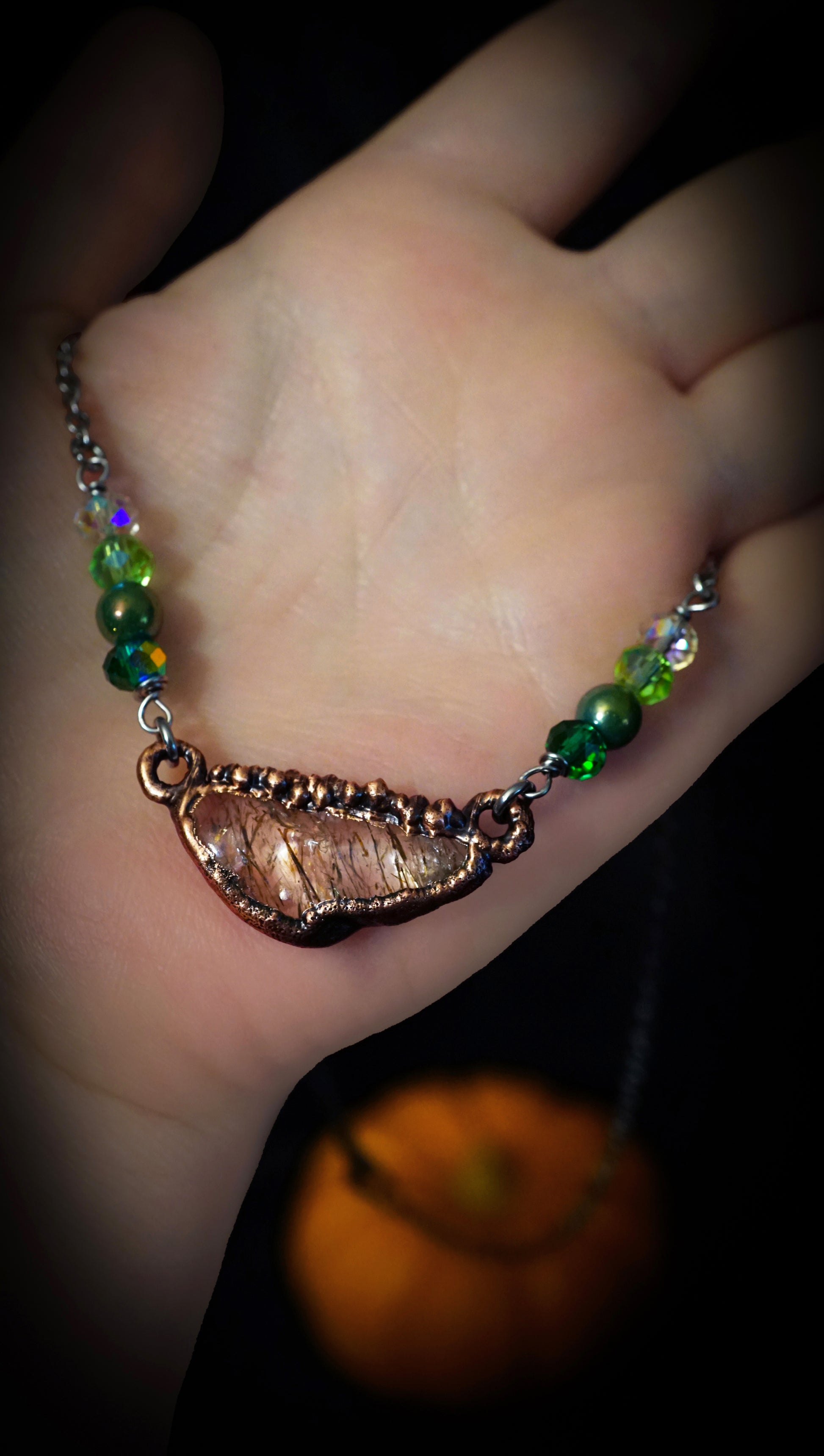 necklace with quartz copper pendant and green beads. in hand with tiny orange pumpkin in background