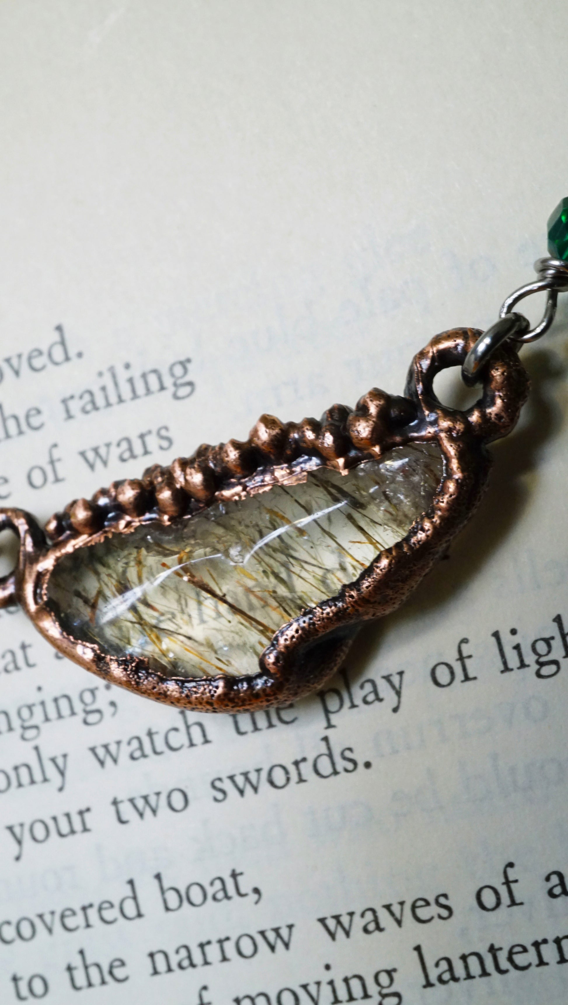 up close picture of rutile quartz, electroformed setting. against an old book.