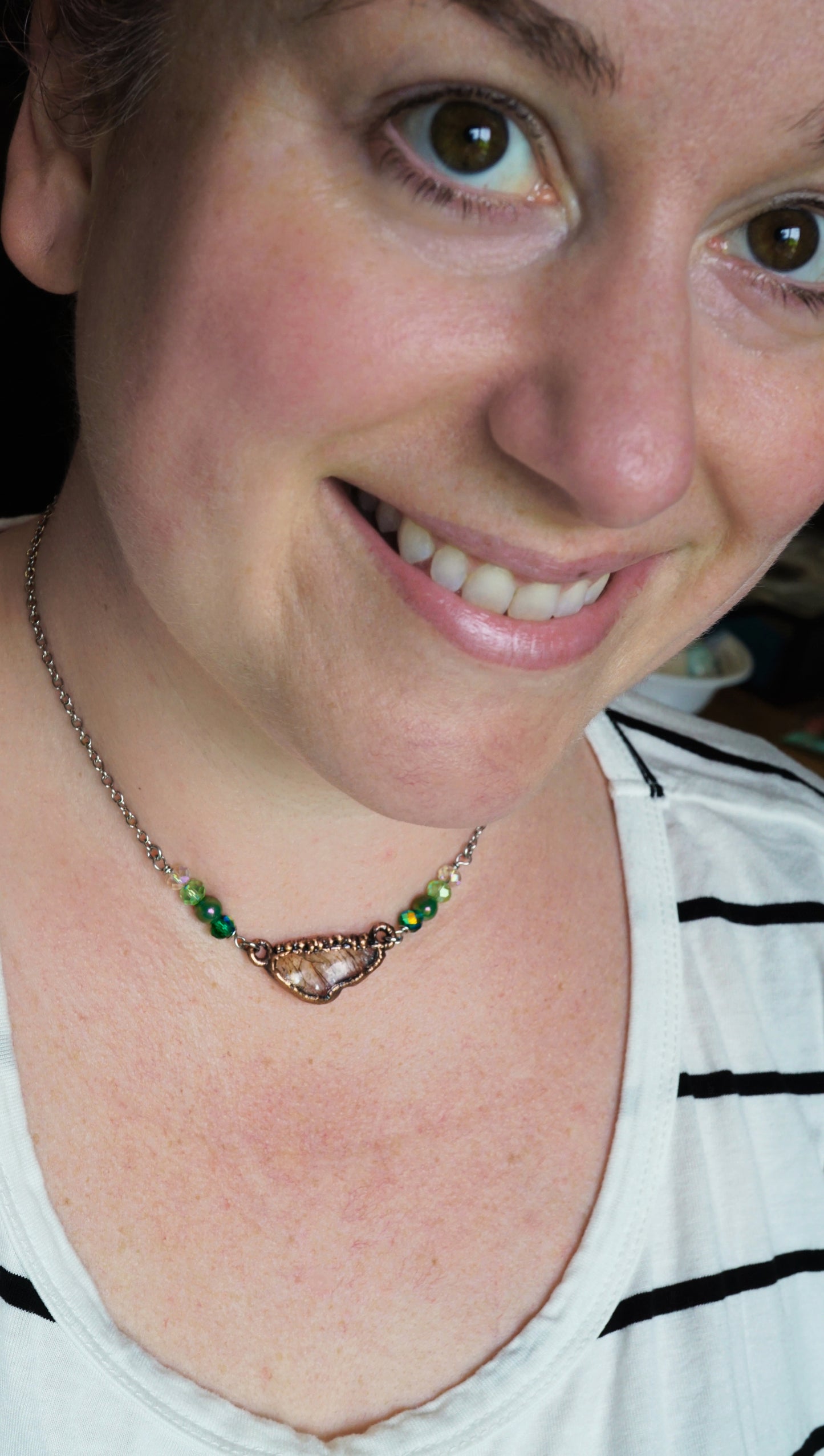 Close-up of a lady wearing a necklace with green beads and quartz crystal in copper.
