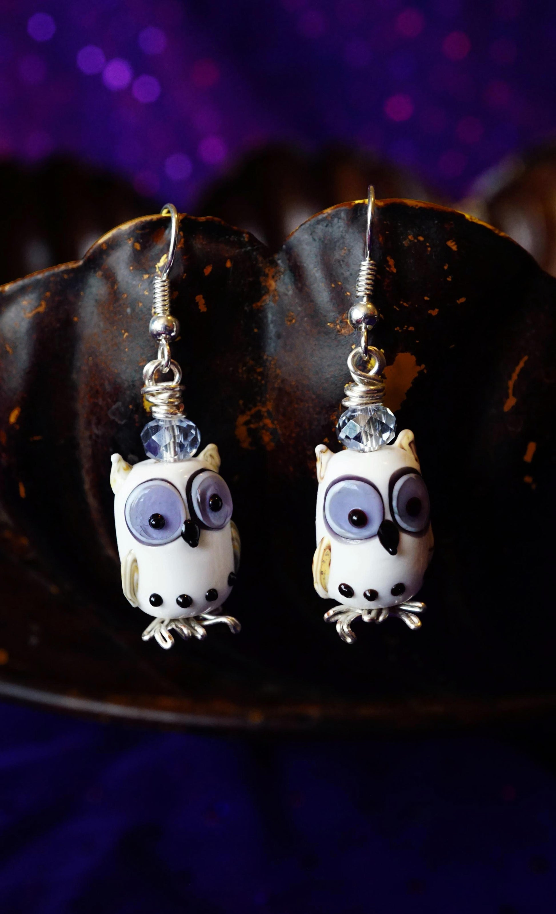 Pair of owl-shaped earrings on a dark surface with a purple background