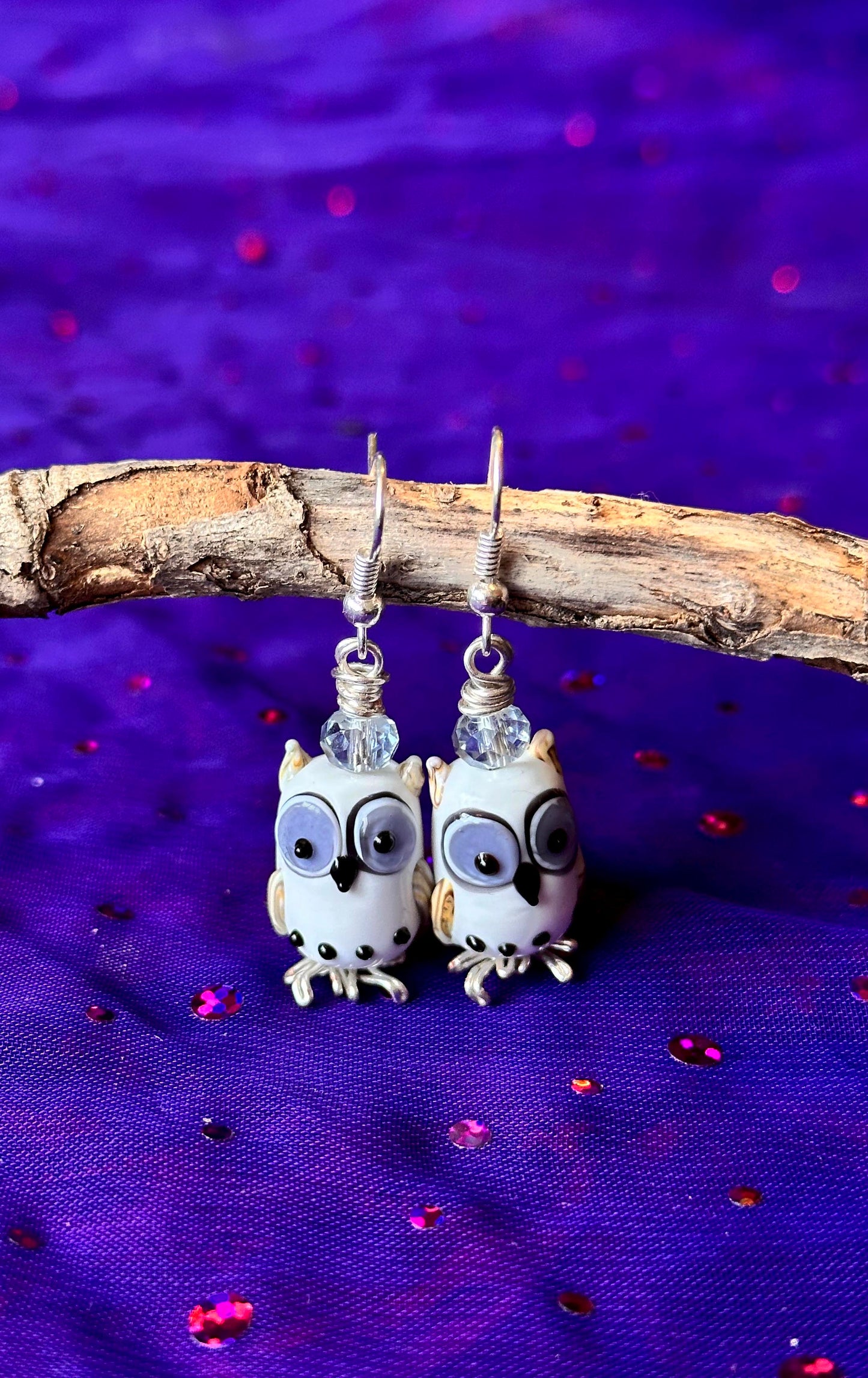 Pair of owl-shaped earrings on a purple fabric background