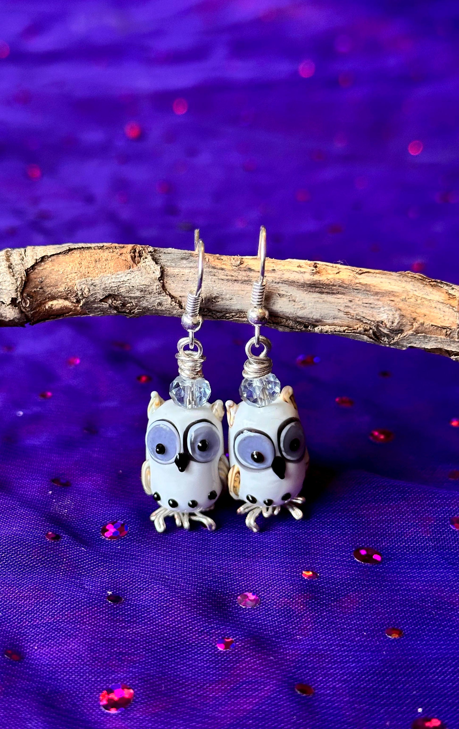Pair of owl-shaped earrings on a purple fabric background