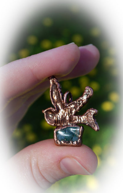 backside of copper sparrow with green moss agate, held in hands with yellow flower and green grass background