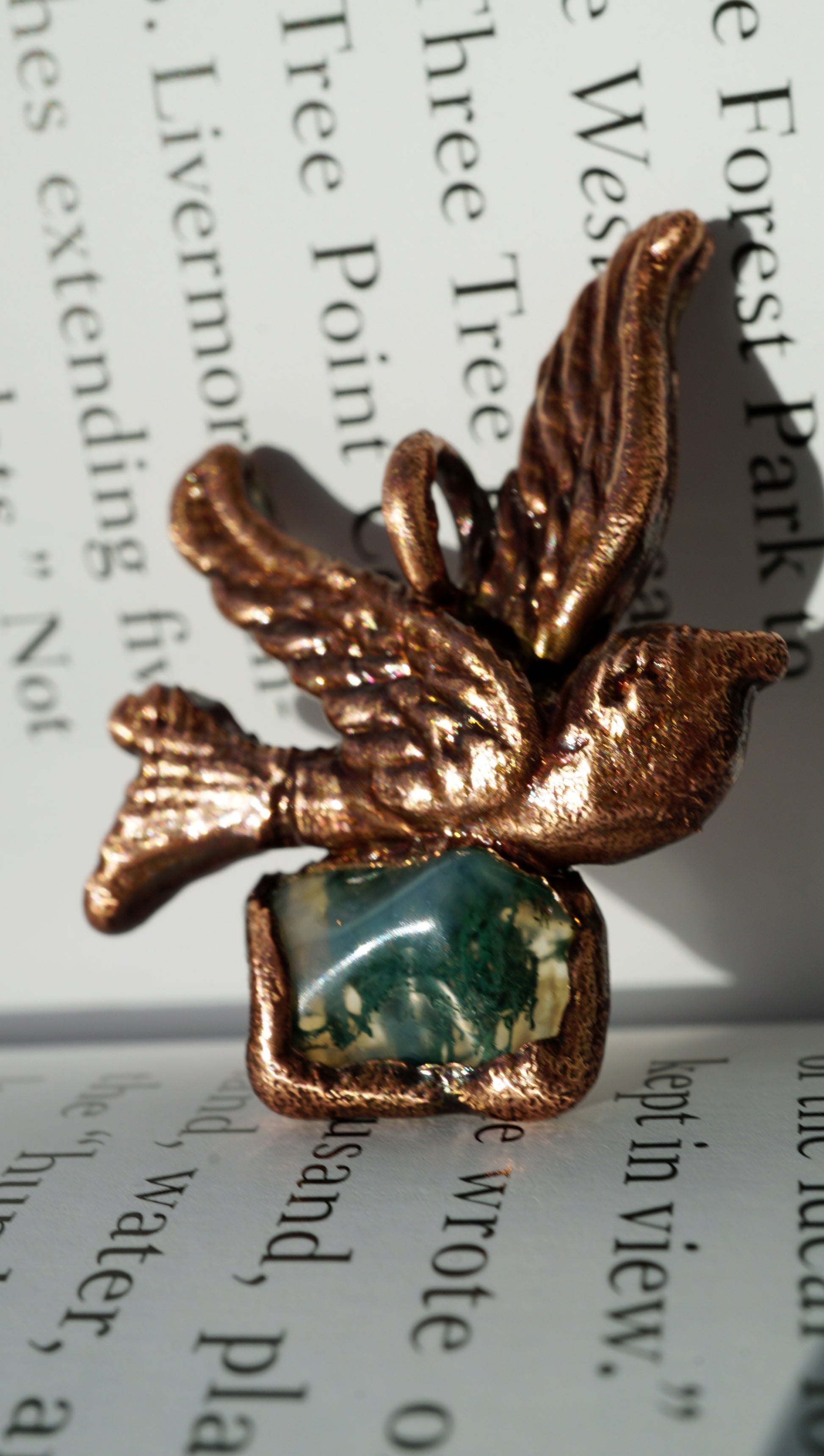 Bronze bird-shaped object with a green stone on a book page