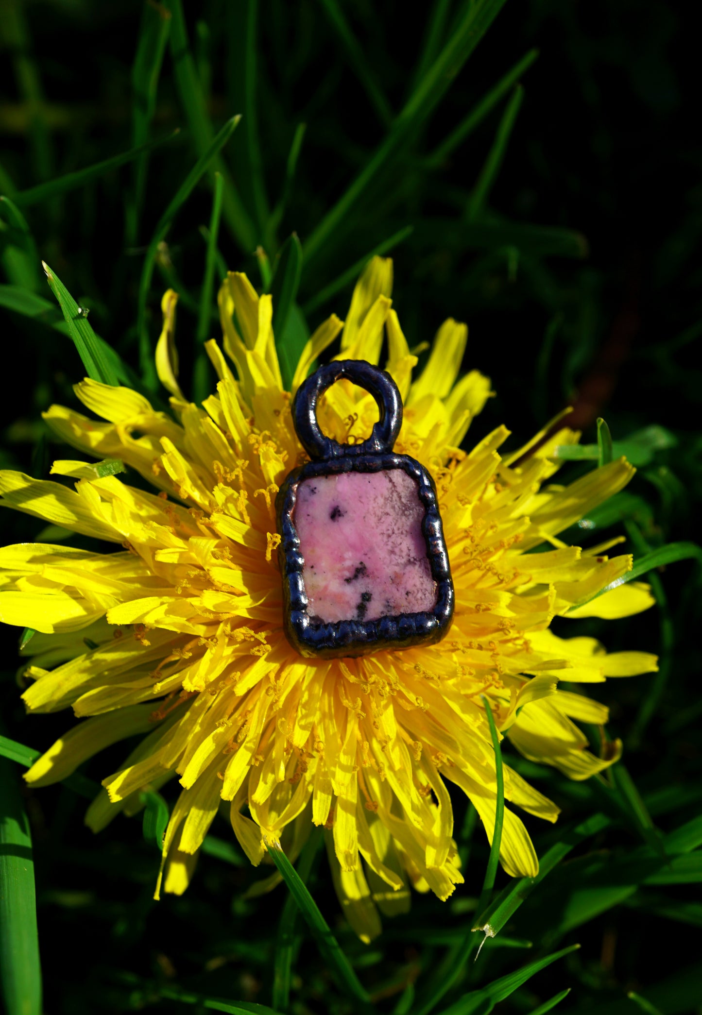 Pink stone pendant on a yellow dandelion flower