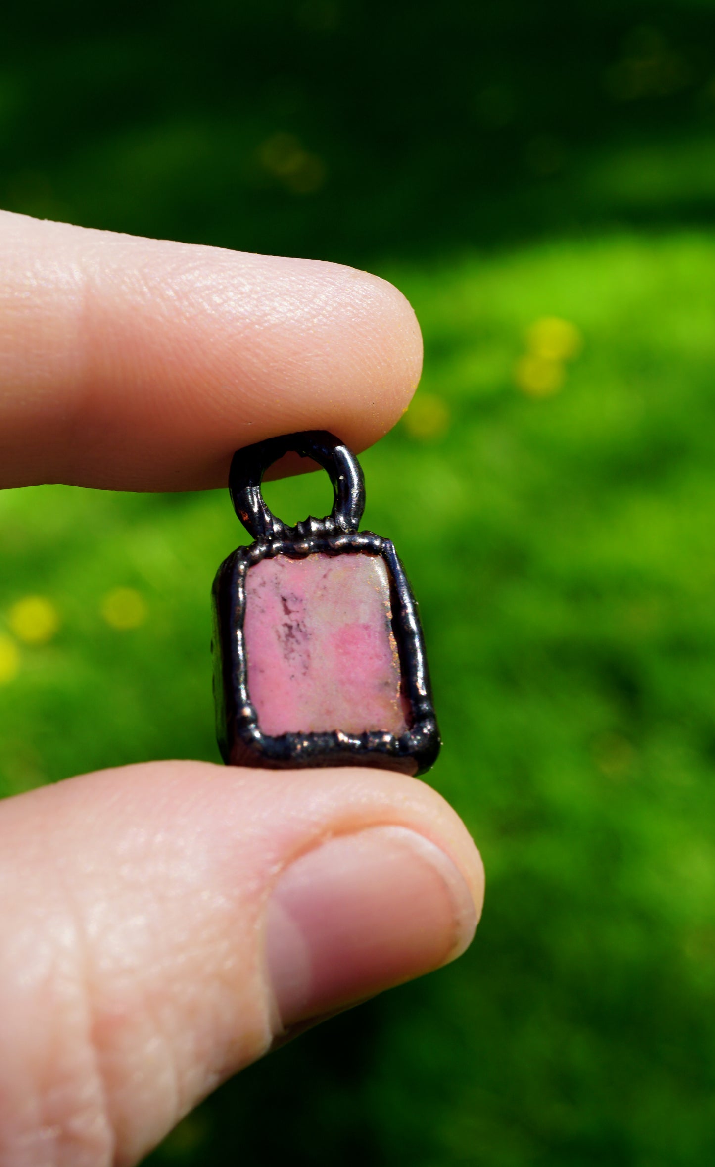 Pink stone pendant held between two fingers with a blurred green background