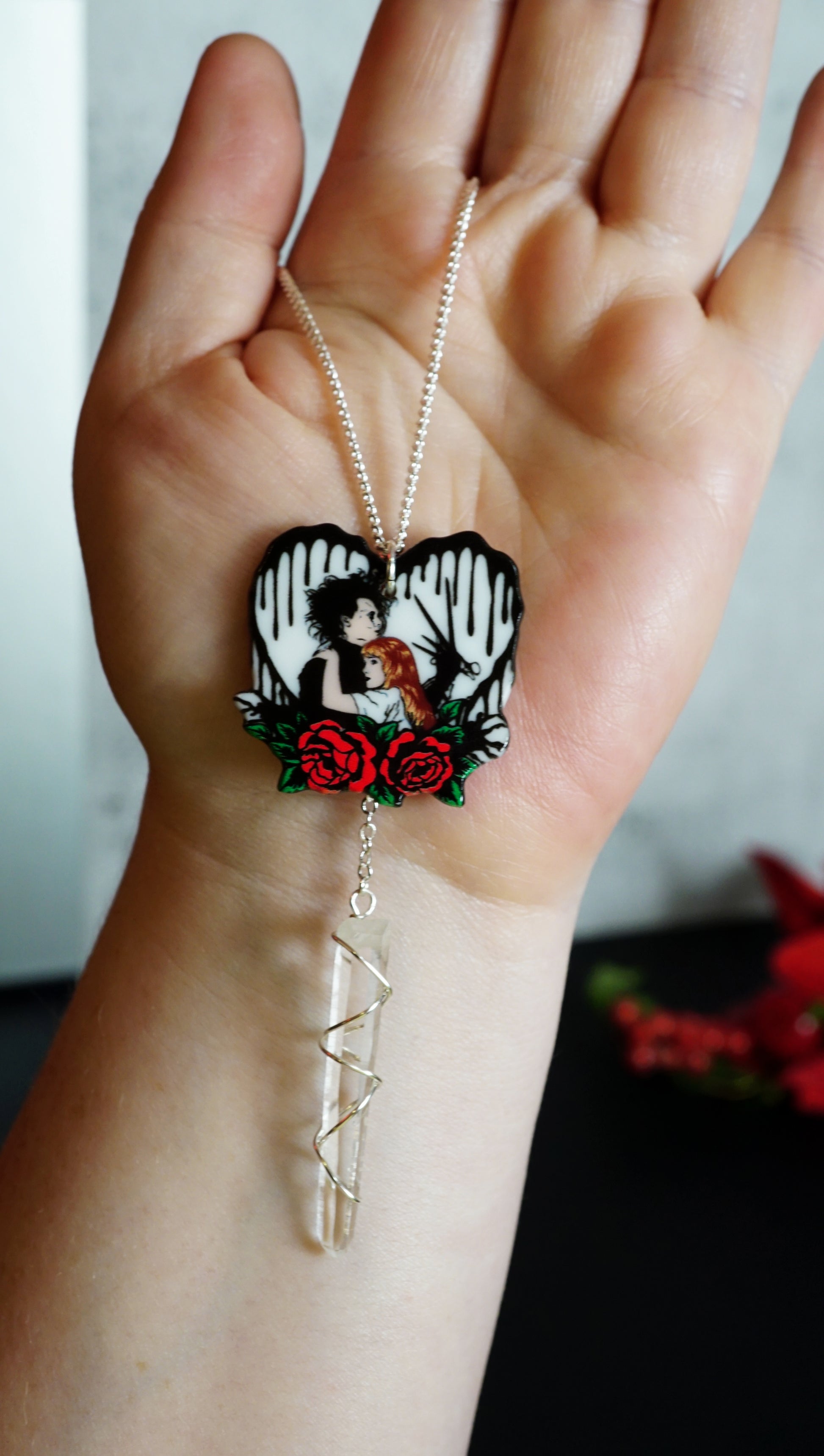hand holding an edward scissorhands and kim necklace. clear quartz drop below. 