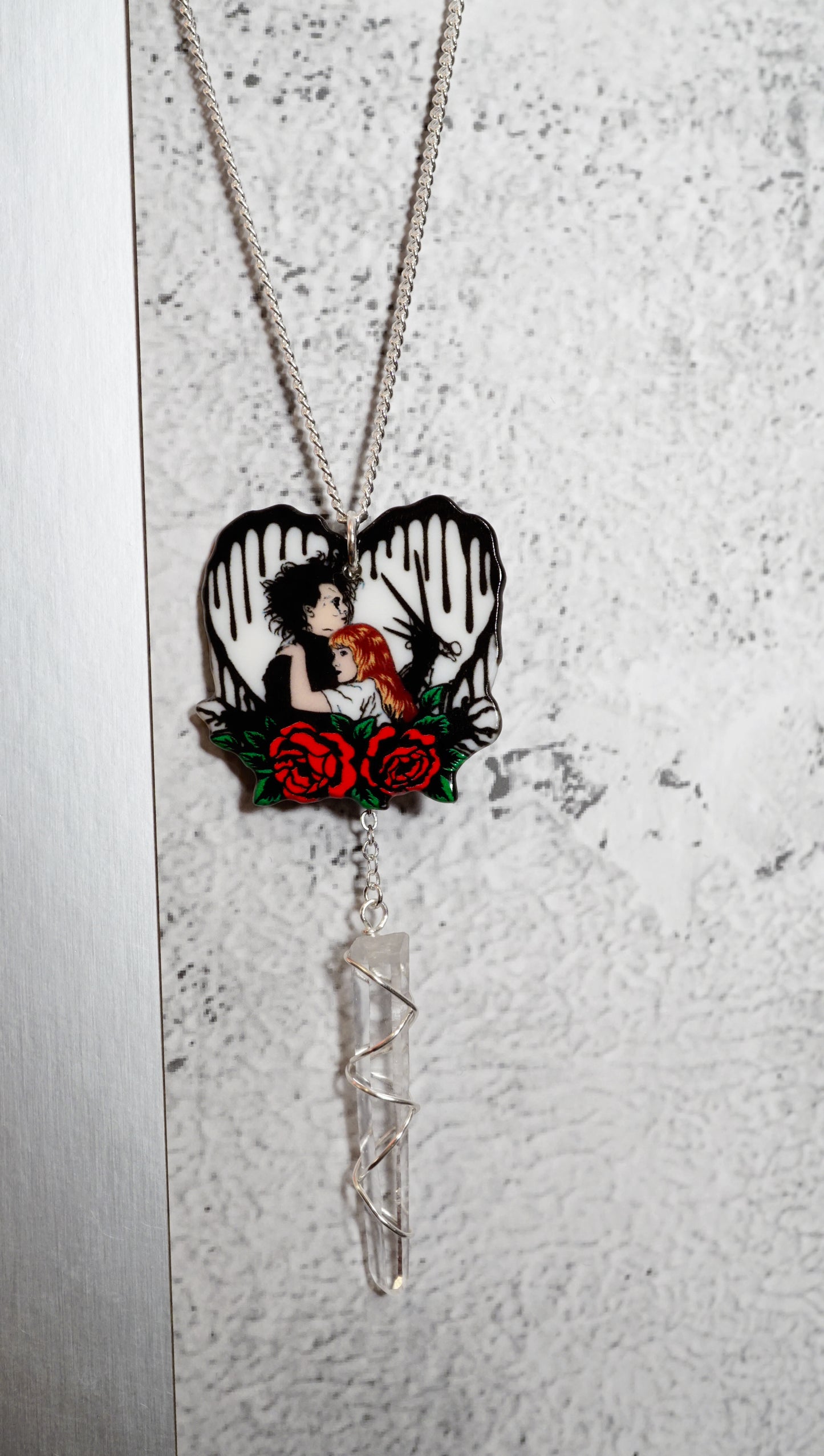 Necklace with a heart-shaped pendant featuring a edward scissor hands and kim. Red roses on  textured white heart with black drops. snowy white background